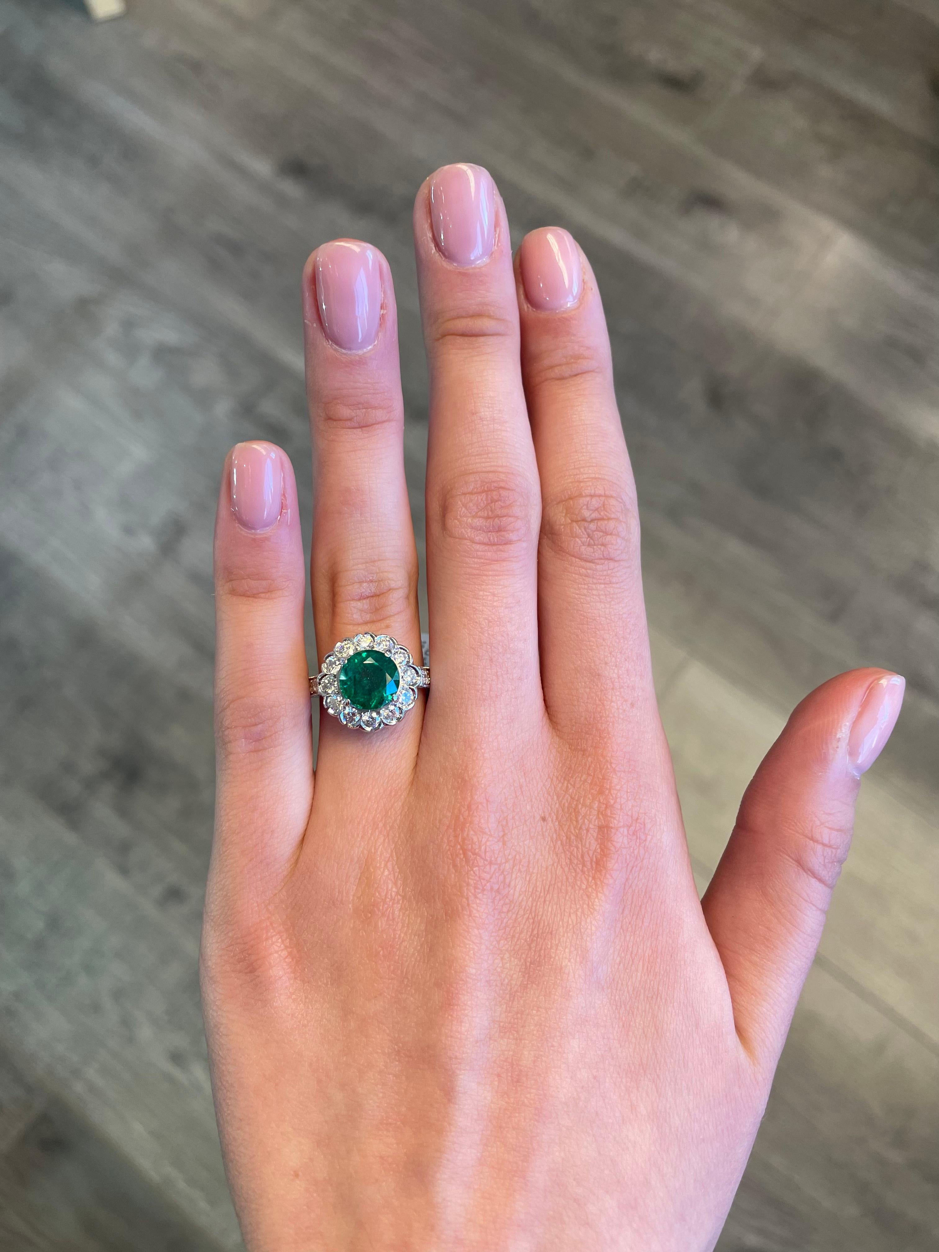 Art Deco inspired emerald and diamond halo ring with milgrain and filigree work.
3.40 carats total gemstone weight.
2.47 carat round cut emerald, apx F2. Complimented by 18 round brilliant diamonds, 0.93 carats. Approximately G/H color and SI