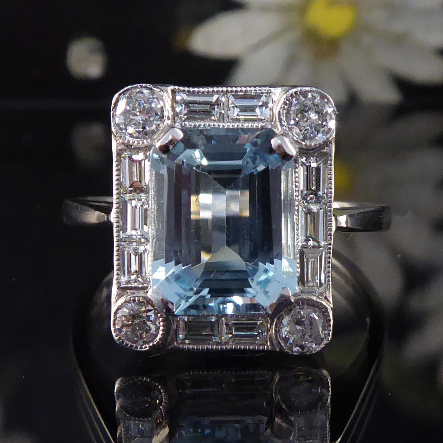 In the Art Deco style, this aquamarine and diamond ring has been created in a stand out design featuring a 2.50 carat aquamarine in an emerald cut to the centre of the geometric shaped cluster.  The aqua measures 9.04mm x 7.70mm x 4.41mm deep and is
