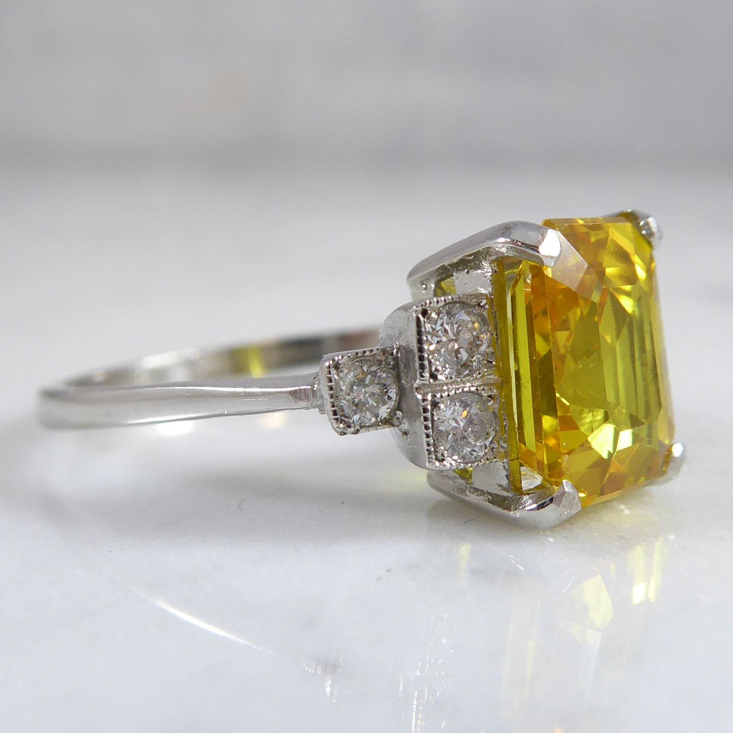 A yellow sapphire and diamond cluster ring in the Art Deco style centring on a four claw set, octagonal step cut, yellow sapphire 2.87ct and measuring approx. 8.53mm x 6.5mm x 4.65mm deep to a white basket style mount.  To each shoulder three round