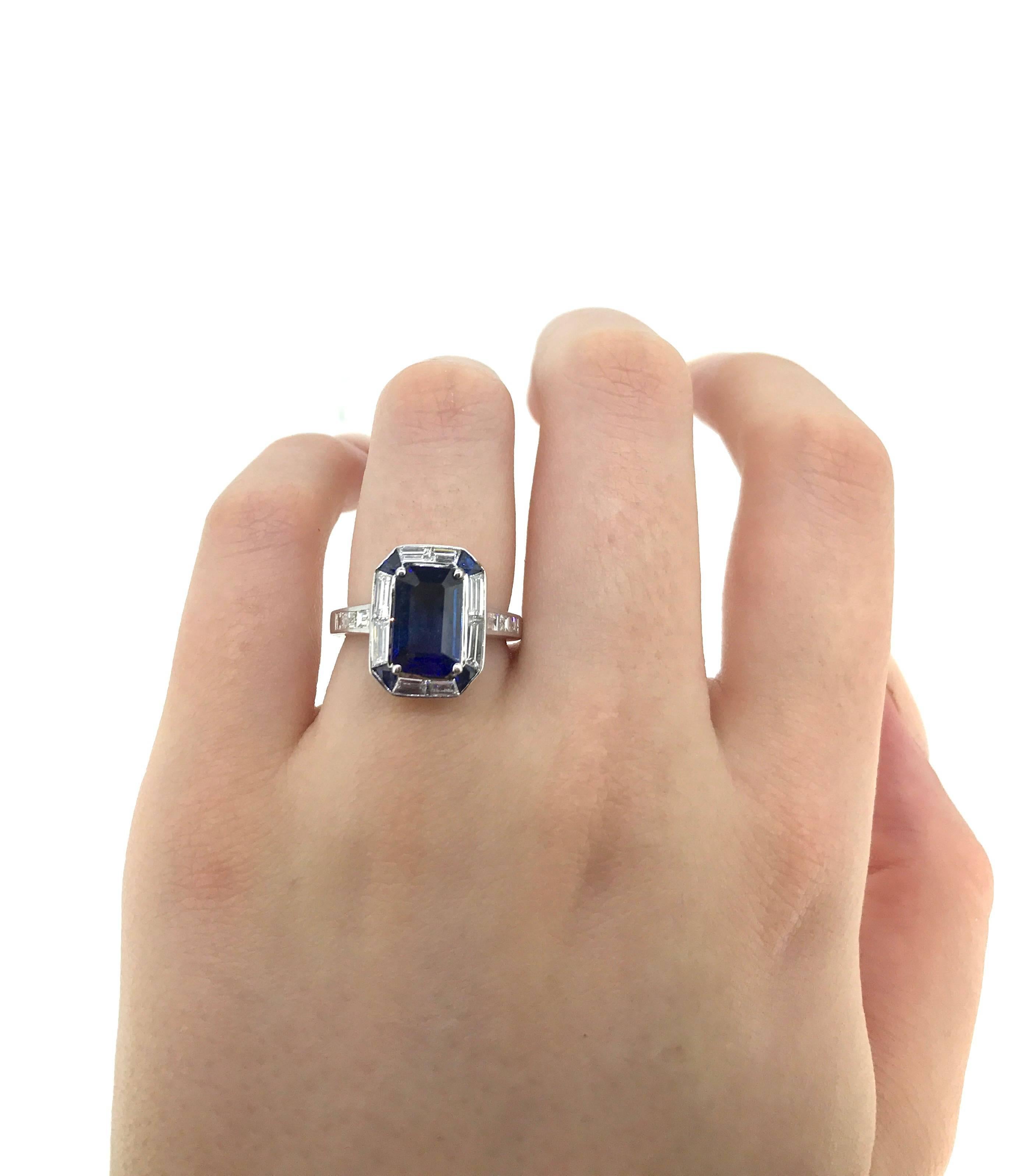 Featuring an 18K white gold modern Art Deco Style ring claw set with an Emerald cut Australian type blue Sapphire 2.53 carat (known weight) (10.21 mm x 6.61 mm x 3.39 mm) surrounded by 4x approx. 10pt. (2.6 mm - 1.3 mm.) trapezoid cut Australian