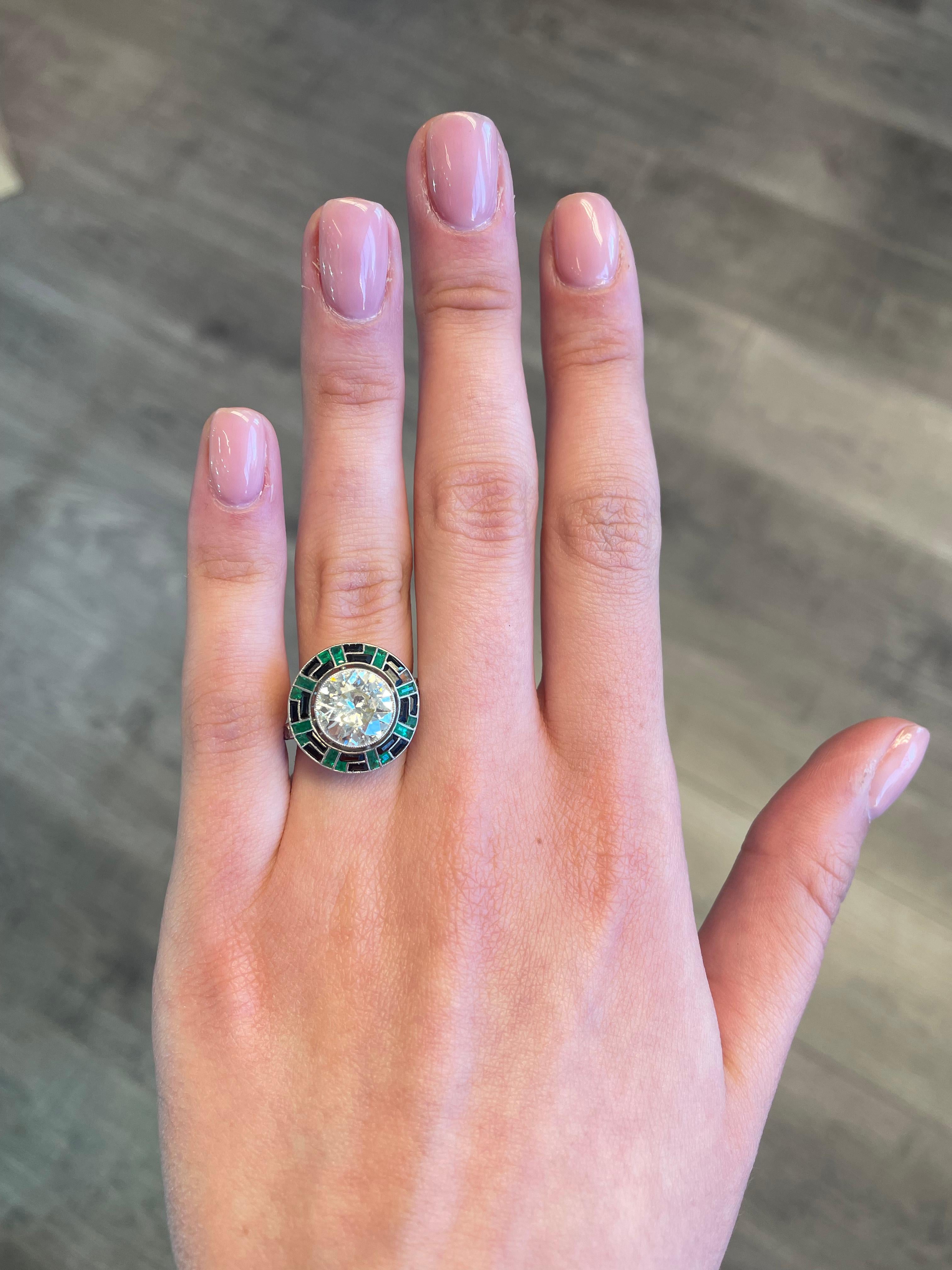 Stunning Art Deco inspired diamond ring with emerald and onyx halo, vintage inspired high jewelry.
Center round diamond 3.32 carats, approximately M/N color and VS2/SI1 clarity. Complimented by custom cut onyx and emeralds apx F2. Platinum, current