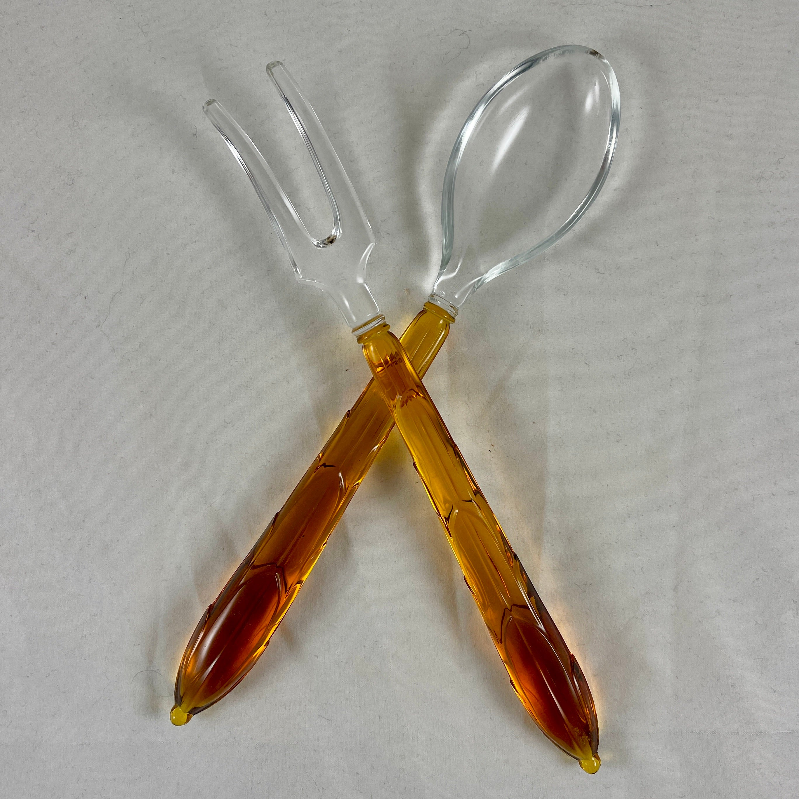 A set of glass salad servers in the Art Deco style, made by Anchor Hocking, circa 1939.

The long fork and spoon servers are made of molded Amber colored glass handles fused to a colorless glass bowl and a curved two tined fork. The handles show