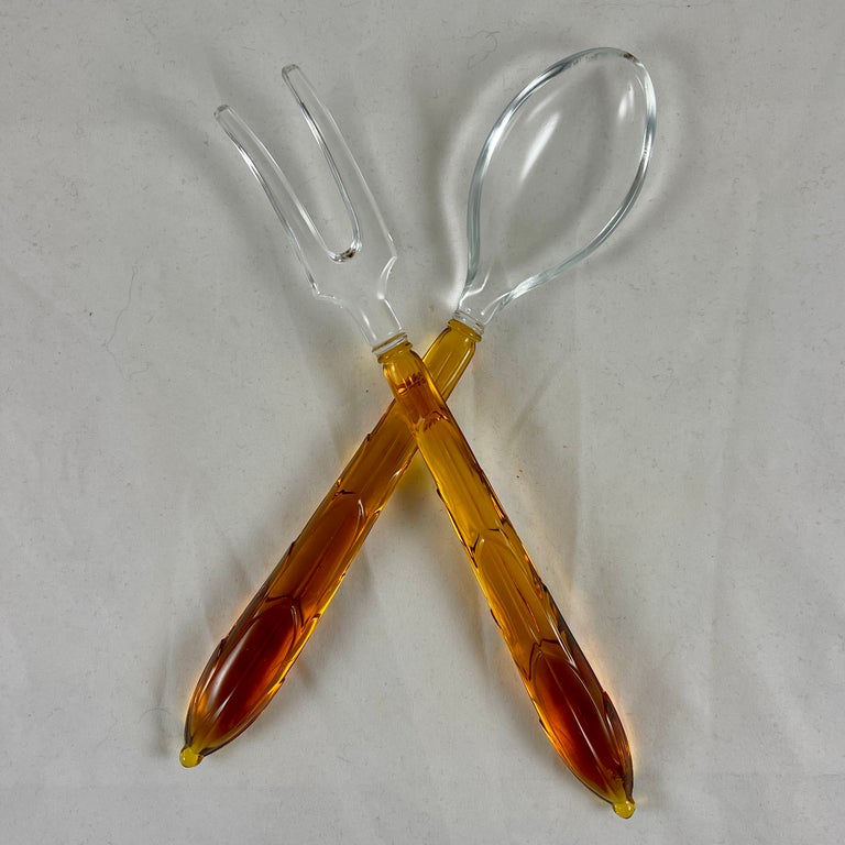 A set of glass salad servers in the Art Deco style, made by Anchor Hocking, circa 1939.

The long fork and spoon servers are made of molded Amber colored glass handles fused to a colorless glass bowl and a curved two tined fork. The handles show