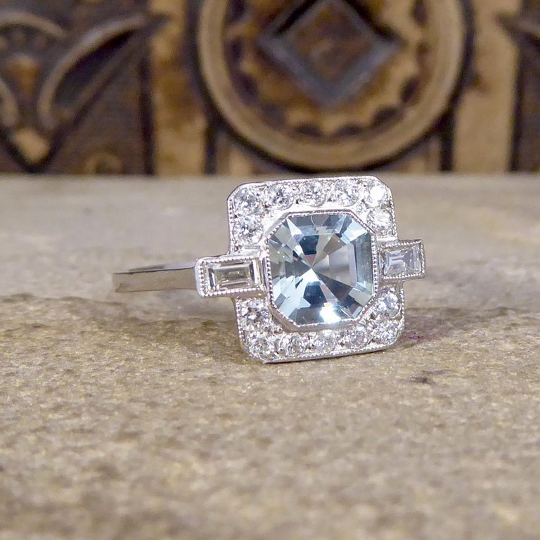This contemporary ring has been crafted to resemble an Art Deco style. It features a single aquamarine weighing 0.80ct in a rub over millegrain collar setting. The beautiful blue Aquamarine is surrounded by a total of 0.33ct round and baguette cut