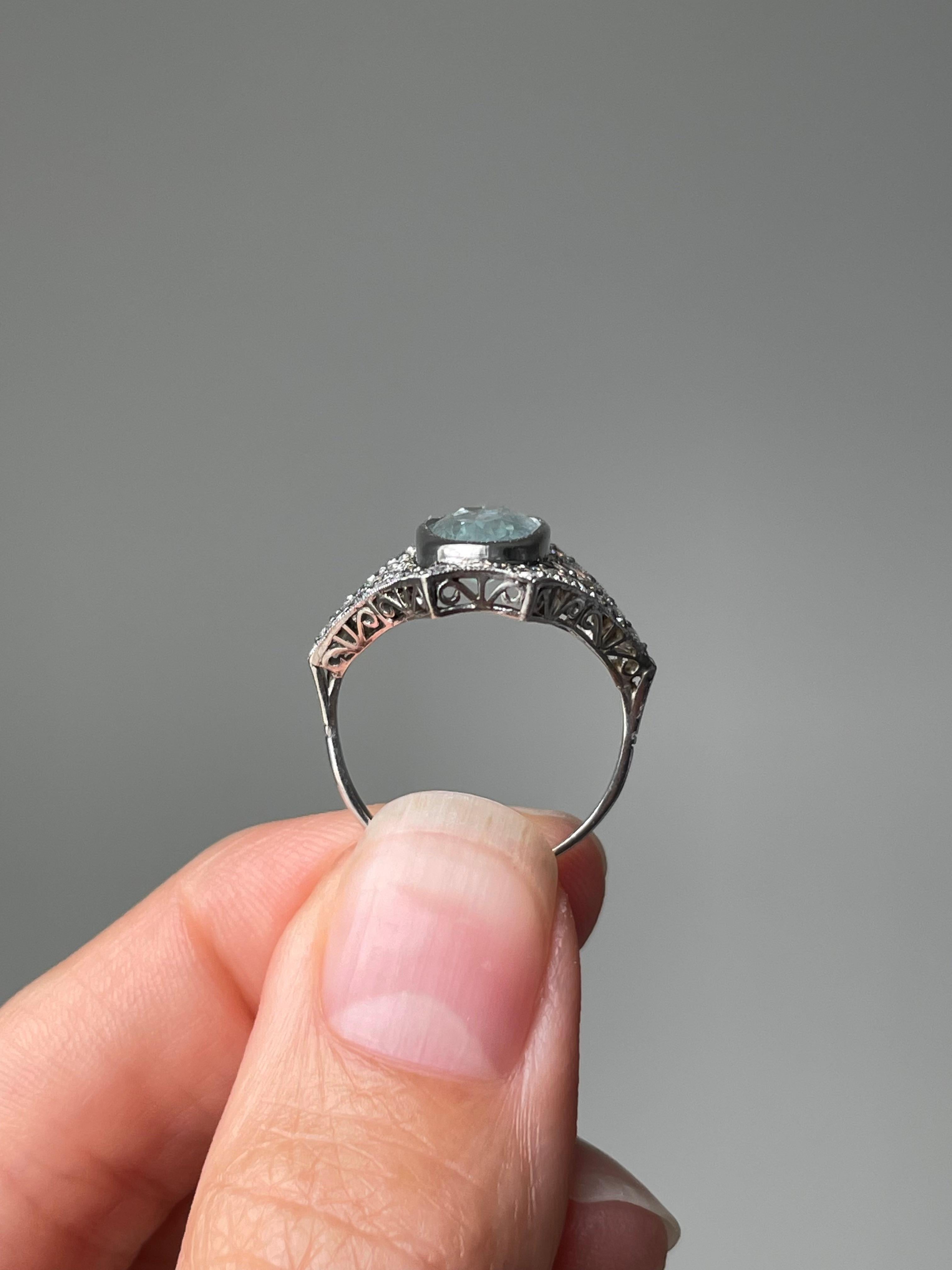 This elegant, finger elongating Art Deco style ring centers on a bezel-set baby blue aquamarine accented east and west by a sparking pair round diamonds, finished with  a sparkling diamond border. Presented in platinum, this ring is exceptionally