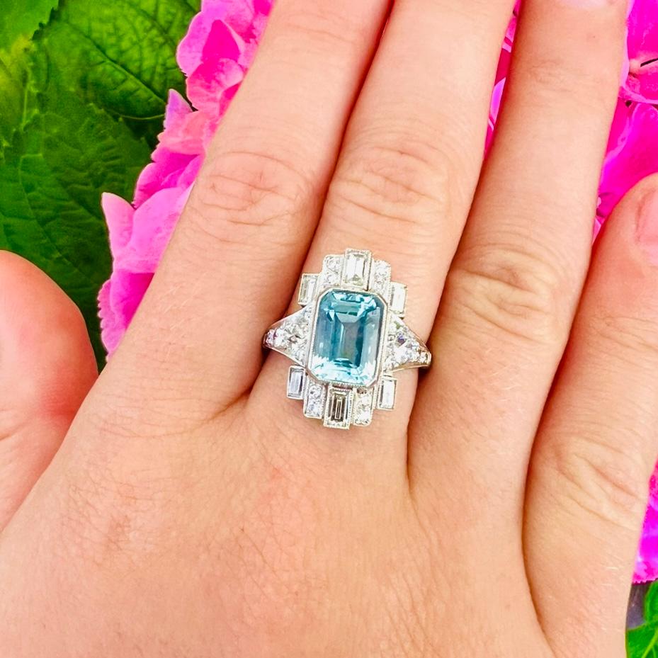 Un beau design art déco ! La bague en platine est ornée d'une aigue-marine bleu ciel taille émeraude pesant environ 6,35 carats, entourée de diamants européens et de diamants taille baguette, pesant au total environ 1,10 carats. La bague pèse 6,9