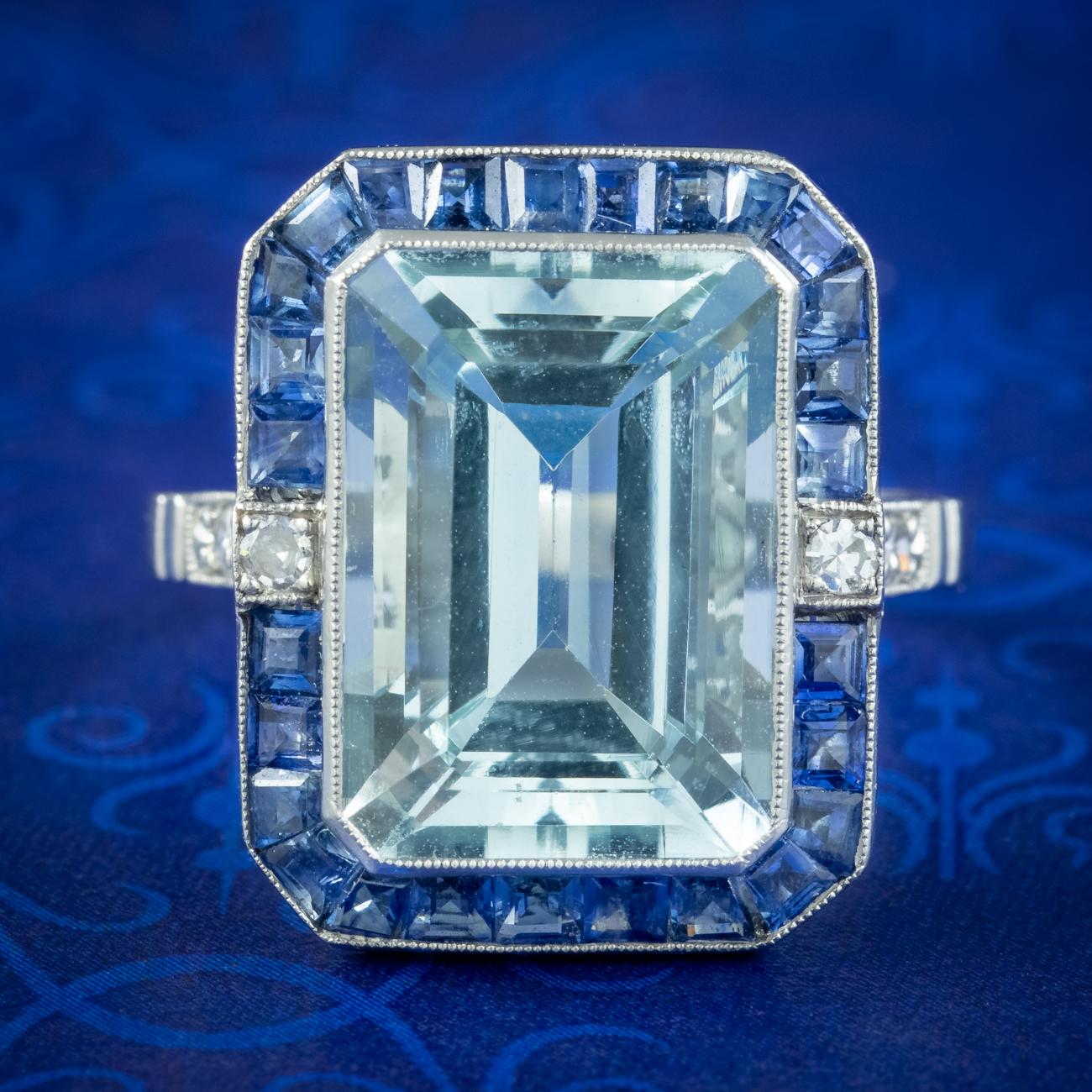 A magnificent Art Deco inspired cocktail ring built around a marvellous emerald cut aquamarine weighed at 7.29 carats. It has a clear glacier-blue hue and is bezel set in a frame of calibre set square cut sapphires (approx. 2.1ct) with diamonds on