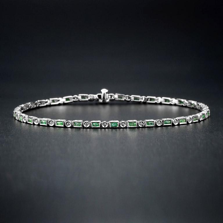 Lujosa y colorida, esta pulsera Aimée presenta esmeraldas verdes baguette alternadas con diamantes redondos talla brillante. confiere seguridad al clásico estilo Art-Deco y un cierre de caja con seguro oculto mantiene segura esta