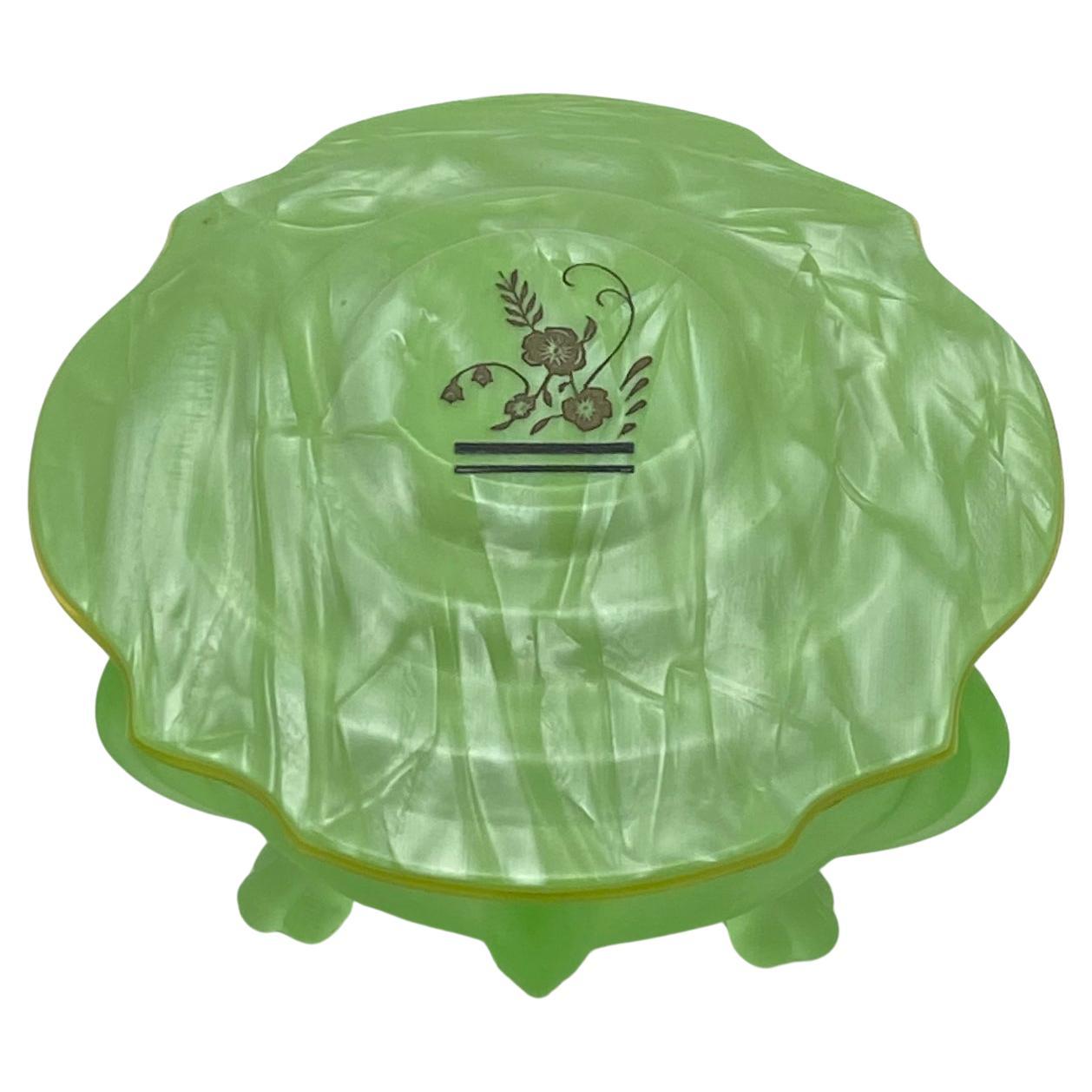 Il s'agit d'une boîte à poudre pour le bain de style Art déco. La boîte a un couvercle en celluloïd avec une partie supérieure marbrée en vert et une sous-couche de couleur ambre. Il a un corps en verre vert nourricier avec trois pieds. La touche