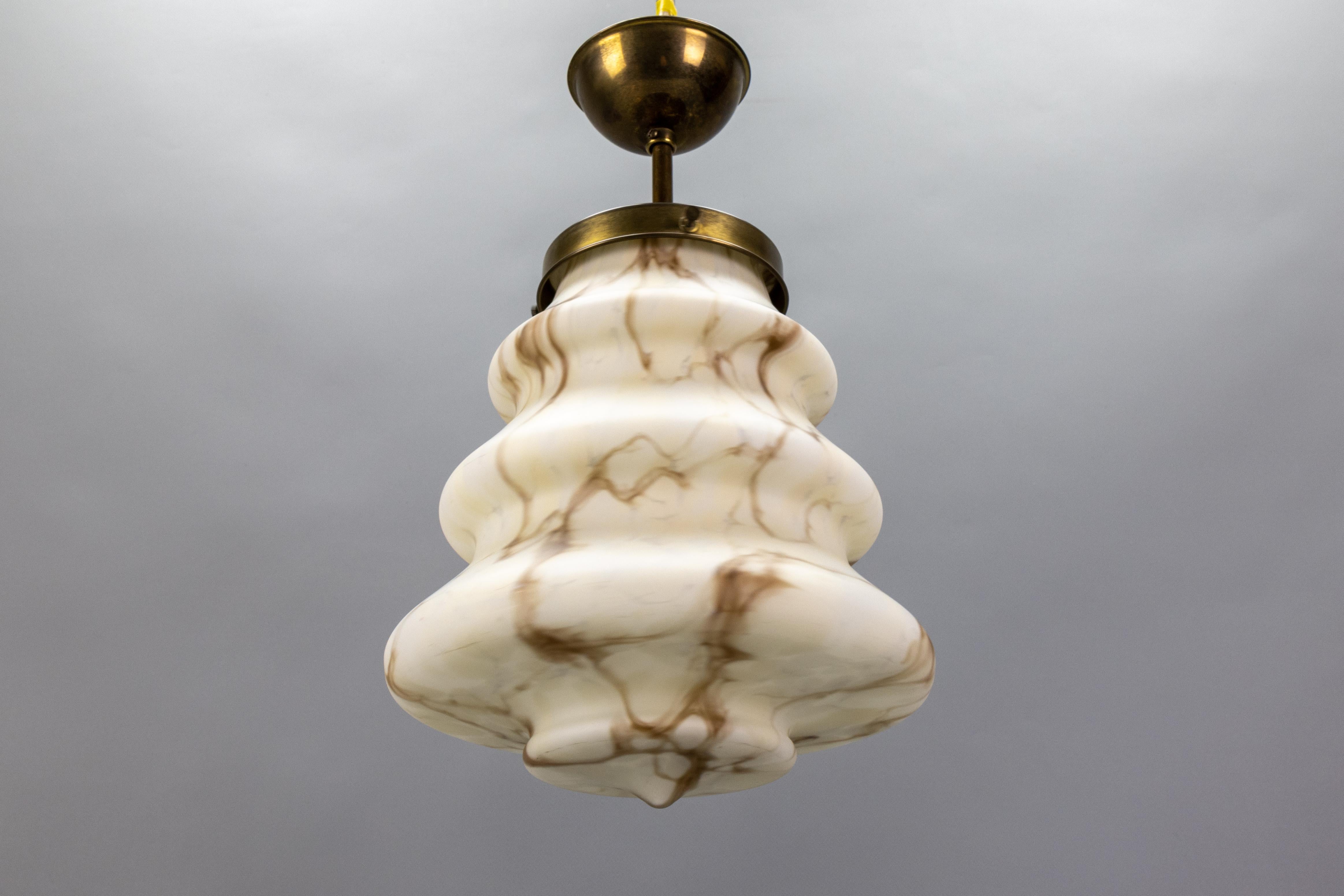 An Art Deco style beige and brown marbled glass and brass pendant light from the 1950s, Germany. 
This adorable ceiling fixture features a beautifully shaped, light beige, and brown marbled glass shade. It is suspended from a brass canopy and