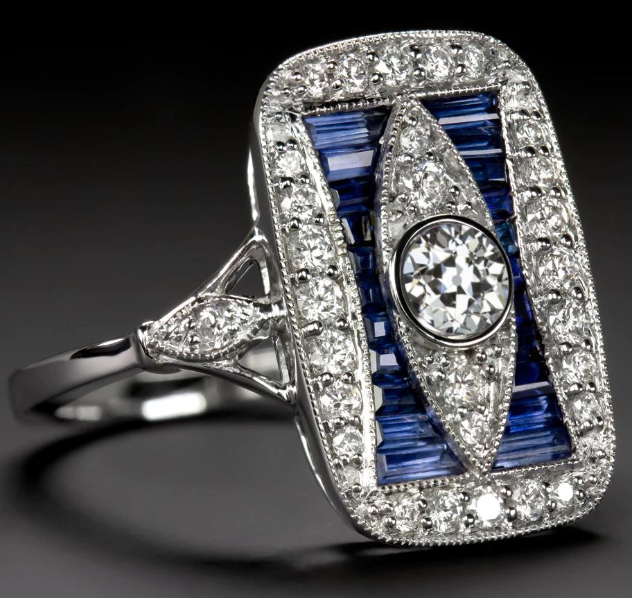 The chic setting is set with brilliantly white and vibrant natural diamonds as well as rich red custom cut natural blue sapphires. Finished with dazzling diamonds and fine milgrain details, this bezel setting provides the perfect backdrop for a