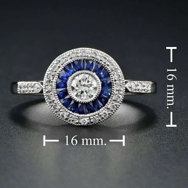This Art-Deco engagement ring is completely spectacular! The vibrant Blue Sapphires is a specialty cut to surround the excellent round brilliant cut center diamond, which is in a thin bezel with mil-grain detail. Crafted in Platinum.
Ring