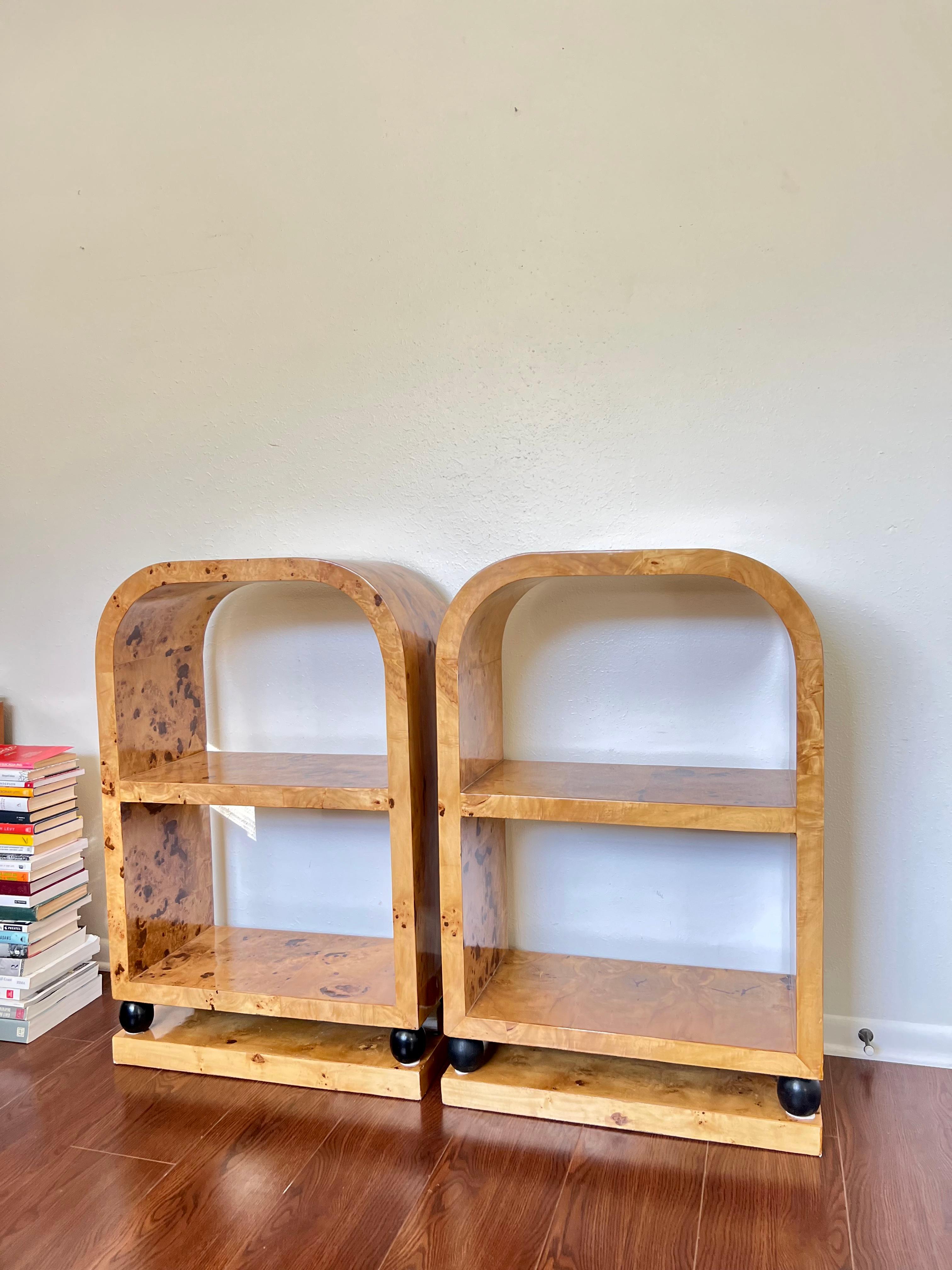 Wonderful pair of Art Deco style bookcases constructed of burl veneer. The arched top open bookcases are finished on all sides, contain three floating shelves, and are raised on ebonized spheres above plinth bases. Overall in very good sturdy