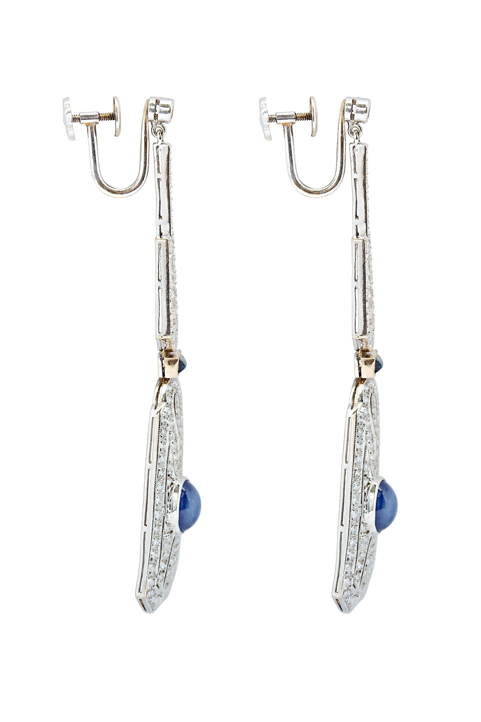 These sensational and beautifully detailed Art Deco style earrings are composed of geometric diamond pave drops each highlighting a bright blue cabochon cut oval sapphire. The drops are suspended by two rectangular cut sapphires surmounted by open