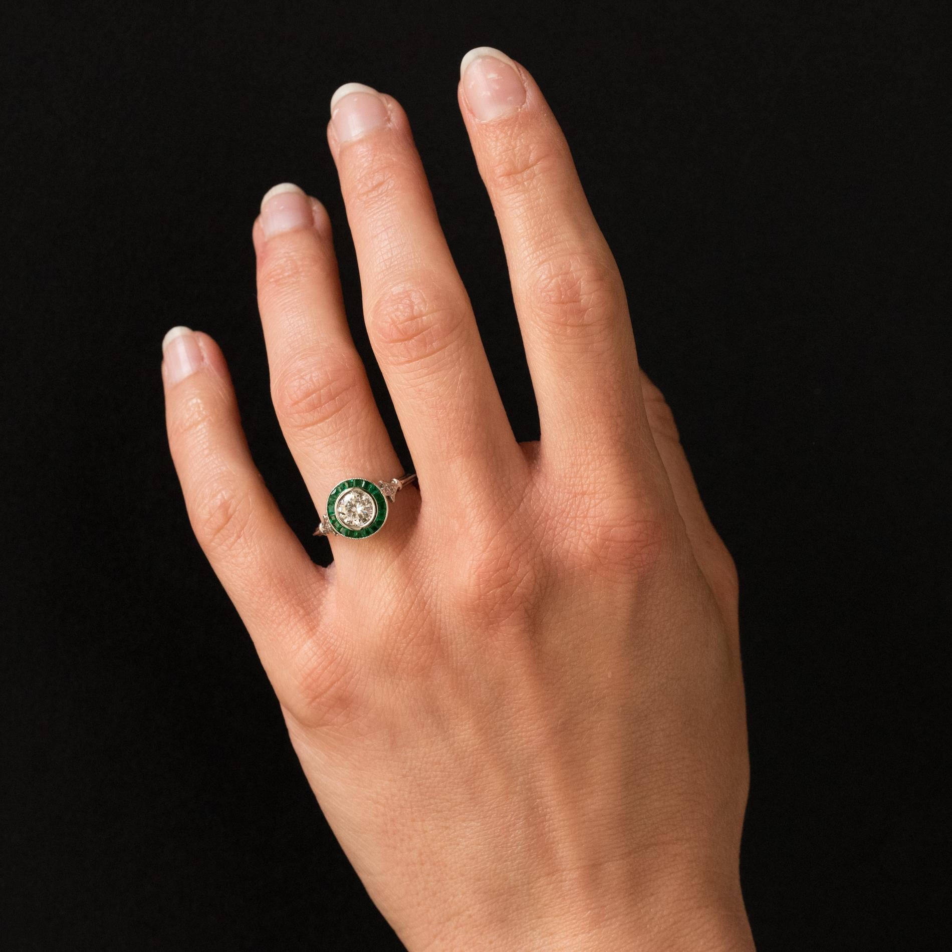 Platinum ring.
Lovely art deco style ring, it is made of a round mount closed set in the center of a brilliant- cut diamond in an entourage of calibrated emeralds. The delicately openwork basket is supported on either side by a small lily flower