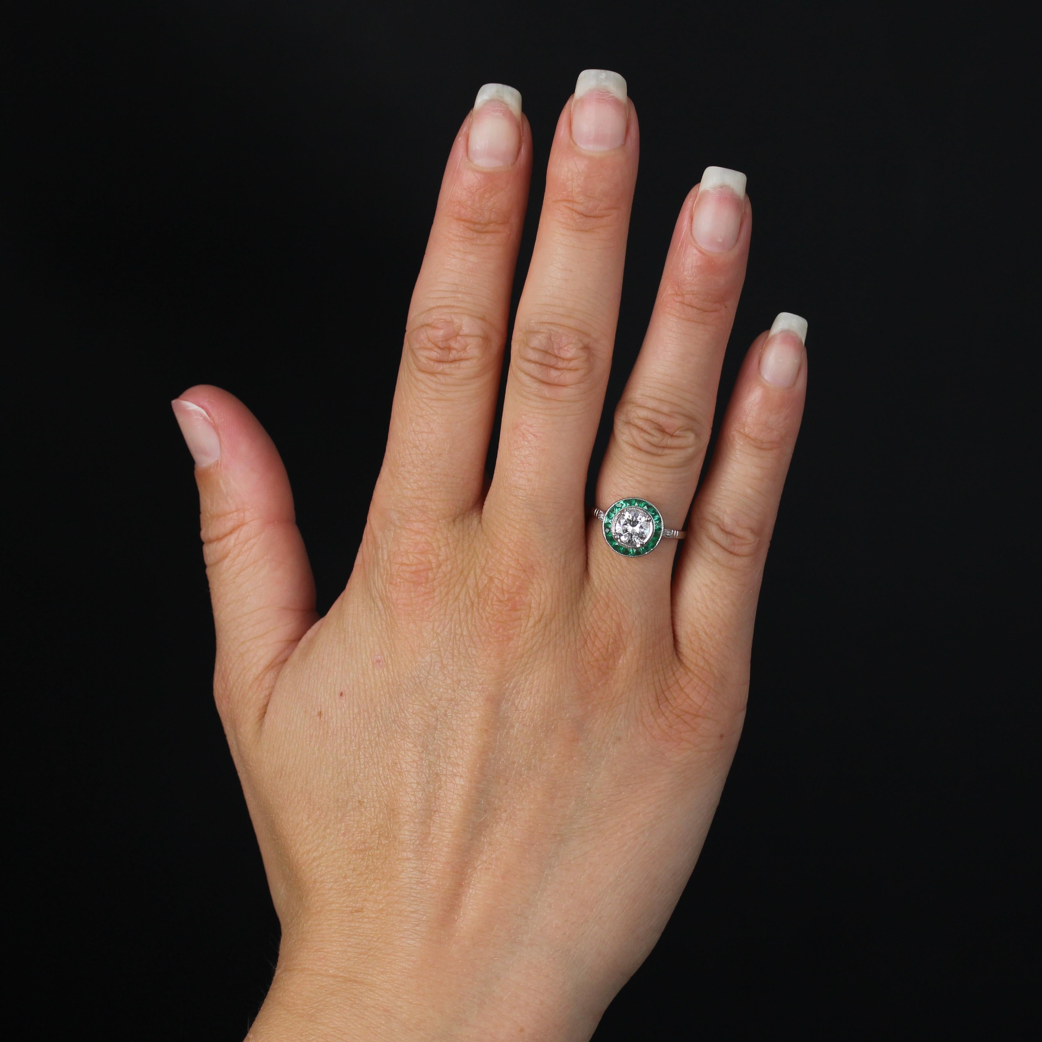Ring aus 18 Karat Weißgold, Adlerkopfpunze.
Der zeitlose Ring im Art-déco-Stil hat eine runde Fassung mit einer Reihe kalibrierter Smaragde in Millegrain-Fassung und einem zentralen Diamanten im Brillantschliff, der von vier Krallen gehalten wird.