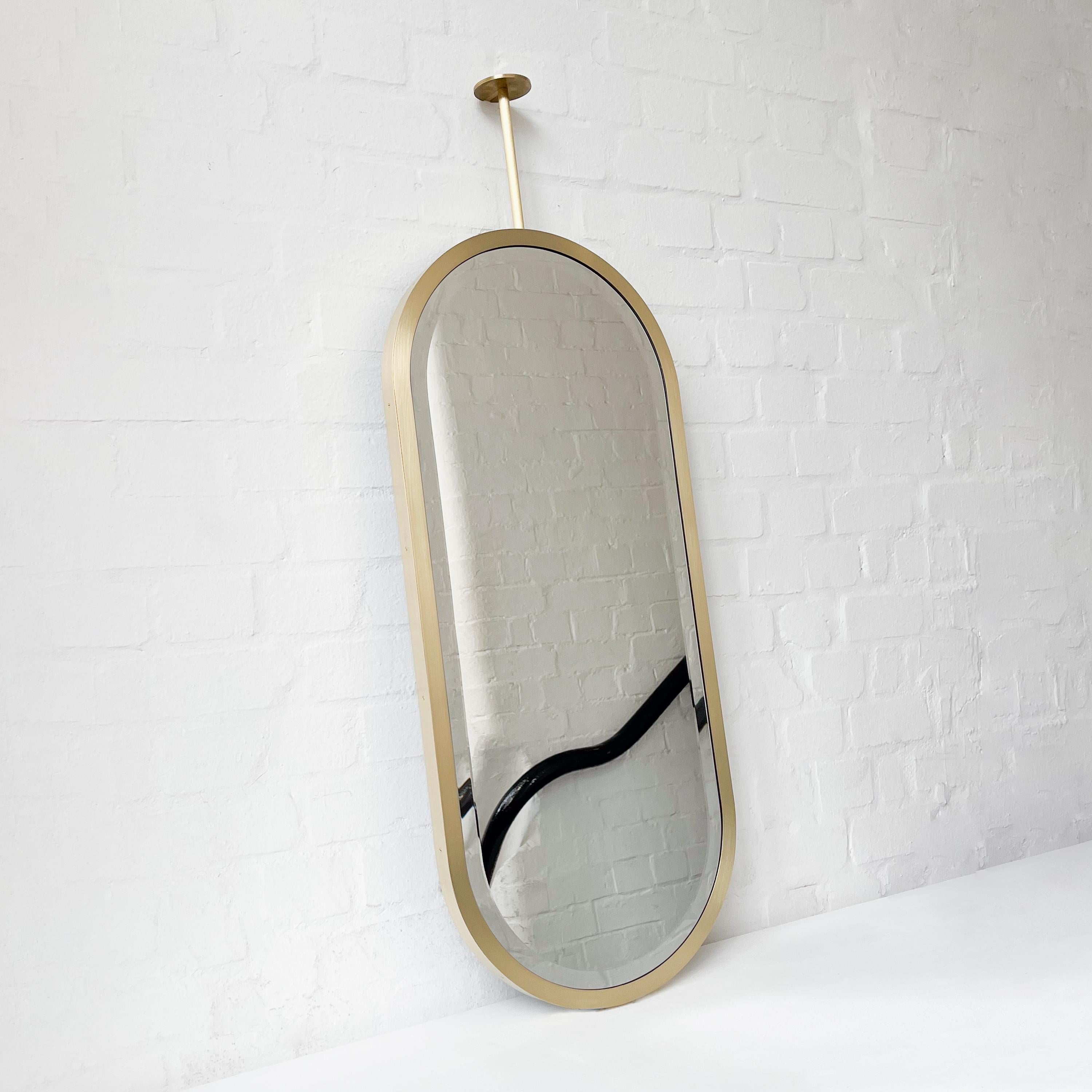 Specchio contemporaneo Capsula™ a forma di pillola sospeso a soffitto con smusso e cornice in ottone spazzolato lavorato a mano.

Dimensioni (personalizzabili):
39 cm L x 90 cm A x 3 cm P / 15,3 pollici L x 35,43 pollici A x 1,18 pollici P.
Altezza