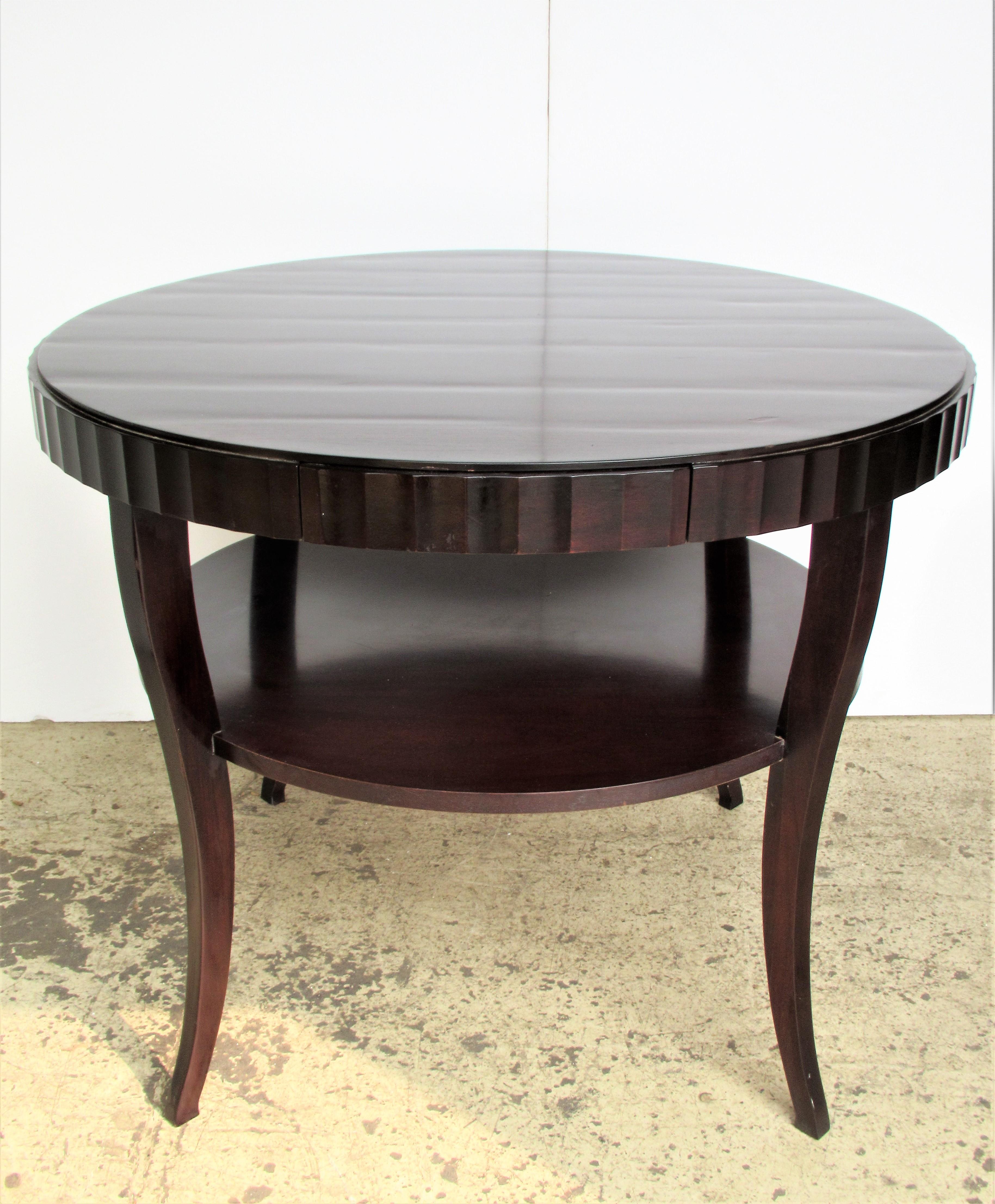 In the 1930s French Art Deco style a Barbara Barry for Baker Furniture one drawer round center table with nicely tapered legs and fluted design apron. The top with a ripple like appearance that gives beautiful dimension to the rich mahogany wood.