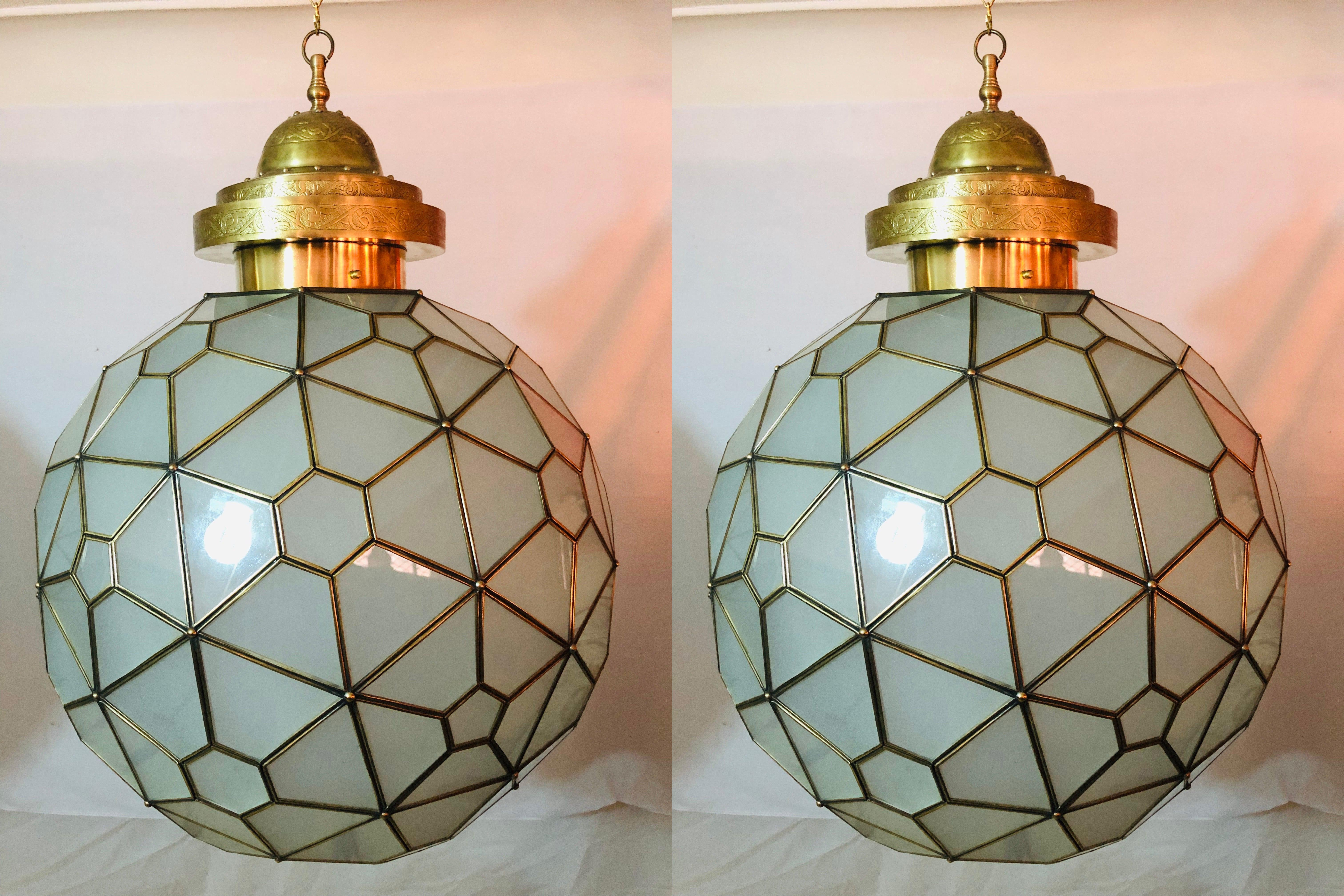 Light up your room with this stunning pair of Art Deco style globe round form milk glass white chandeliers or lanterns with brass inlay and handcrafted with filigree design canopy. Recently wired setting housing two bulbs.
These fine custom lanterns