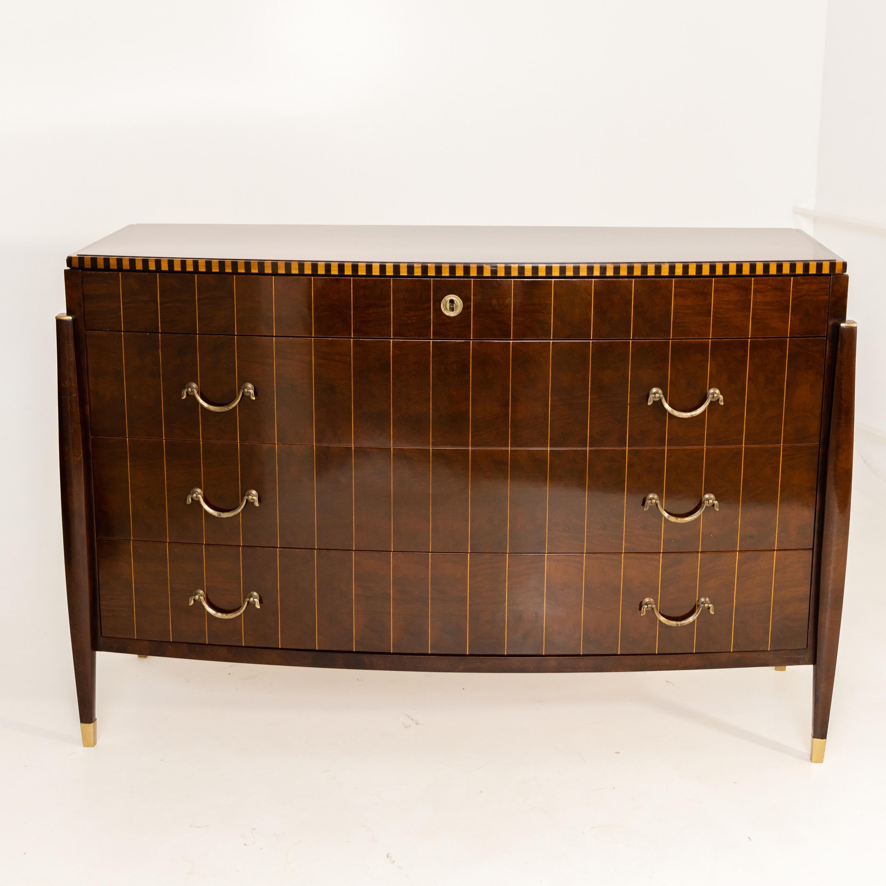 Four-drawer dresser with slightly curved front and accentuated tapered legs with brass decorations. The top panel is accented by a light-dark edge and the body is articulated by light thread inlays. The dresser has been expertly restored and hand