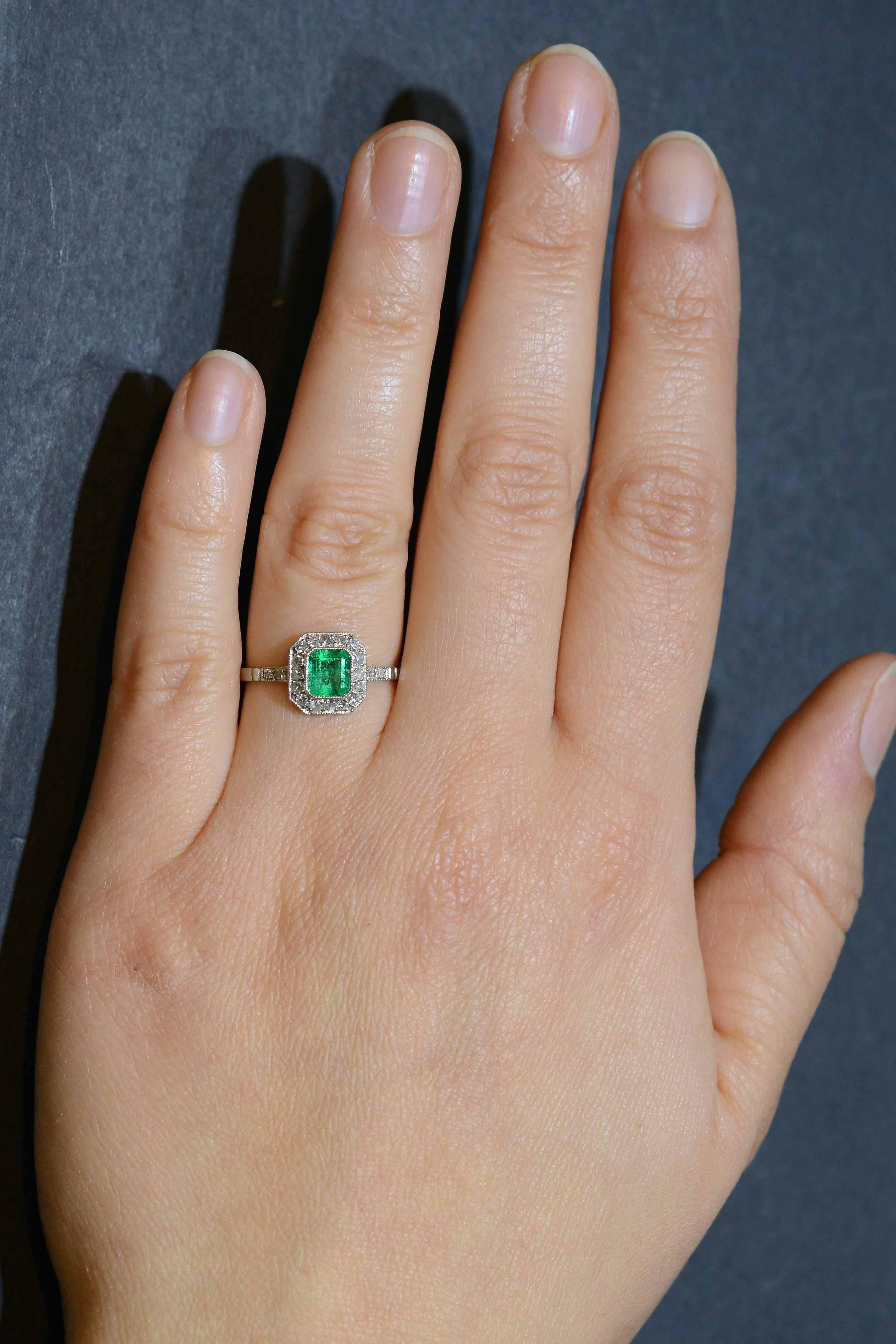 A breathtaking grass-green emerald takes center stage in this striking Art Deco style engagement ring. The platinum setting features a gemstone that glows with a light from within its soul. Floating in a bezel setting and surrounded with a dainty