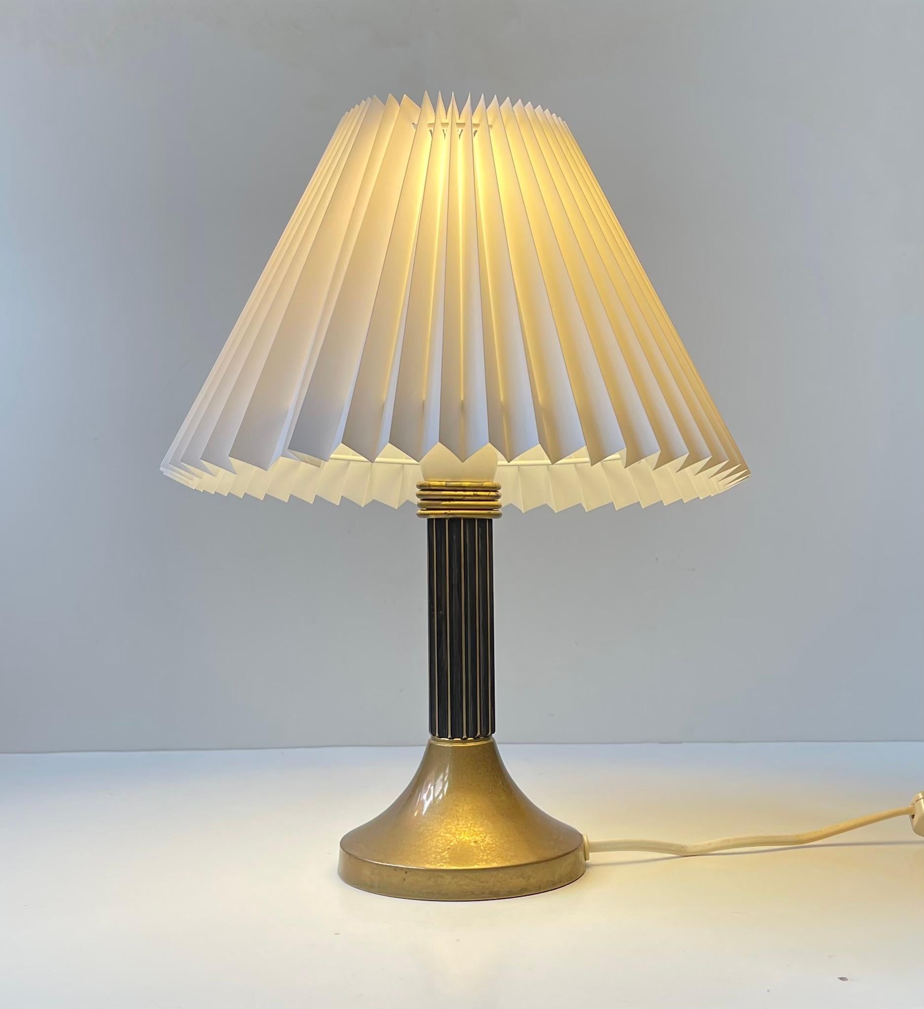 Lampe de table Art Deco revival exécutée avec une tige de colonne en laiton cannelé et 3 anneaux remontant vers sa douille. Elle est montée avec un nouvel abat-jour danois blanc cannelé et dispose d'un interrupteur marche/arrêt sur son cordon.  