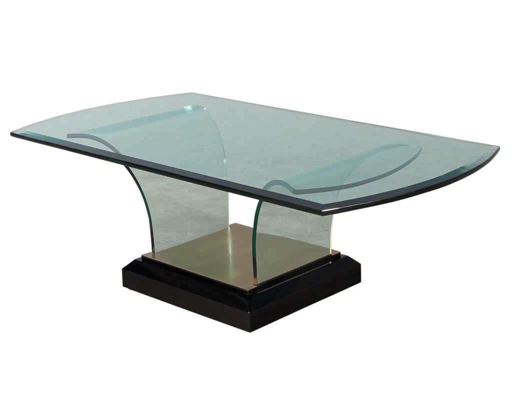Art Deco curved glass coffee table. Art Deco inspired table with curved glass pedestal design and metal brass detail. Resting on polished black lacquer base. Top glass has a bevelled edge, all original with minor scratching consistent with age and