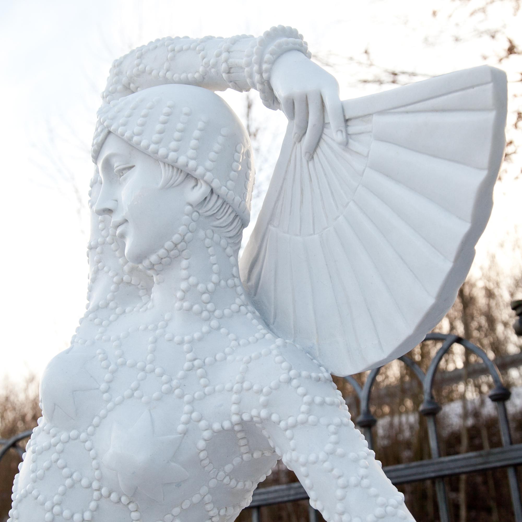 Marble sculpture of a fan dancer in a costume with beaded pearls. The sculpture was hand-carved out of white marble and has a very fine surface.