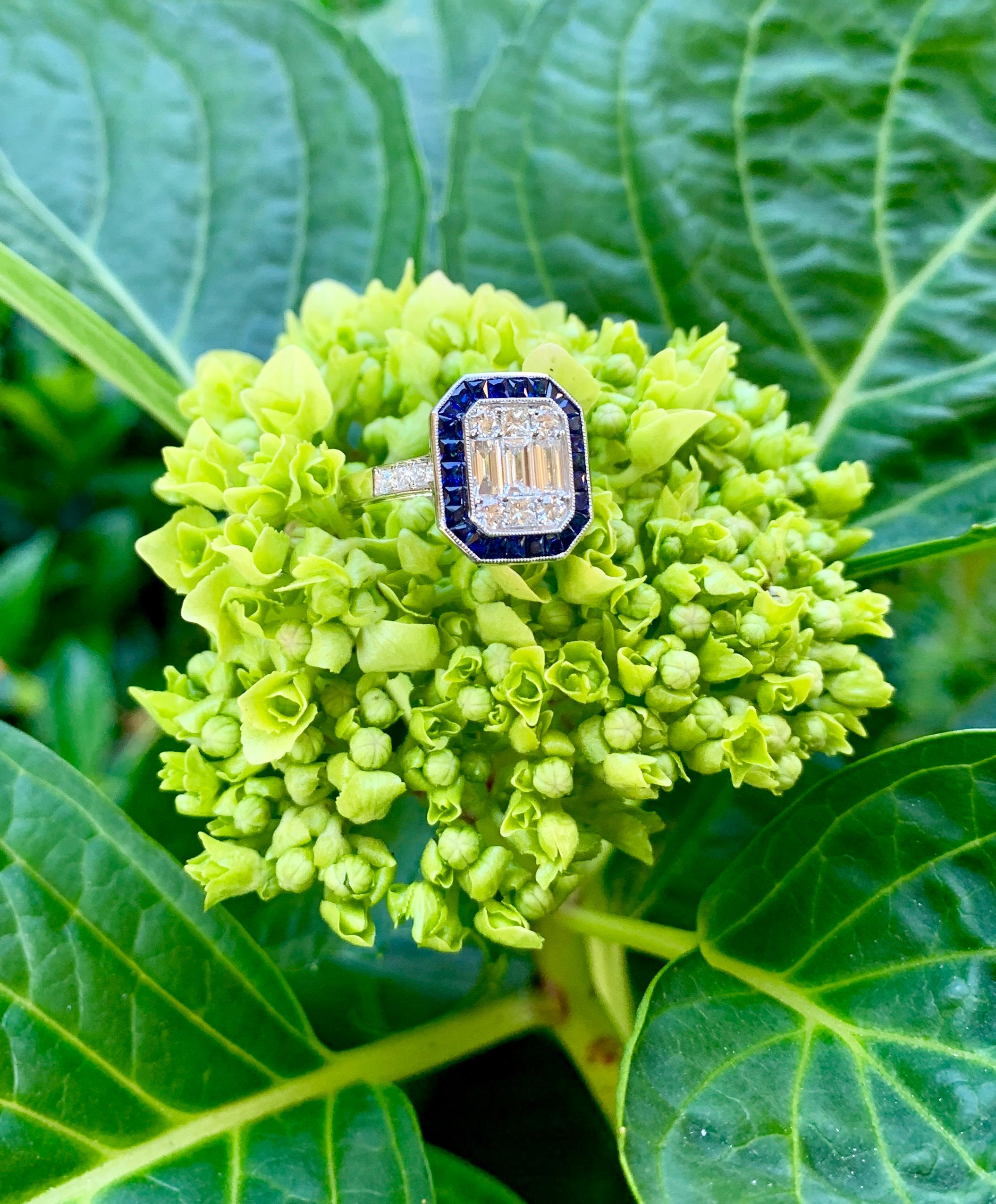 Invisibly set baguette and shared prong set round diamonds give the illusion of a very large, cut corner rectangular step cut stone in the center of this beautiful ring. The center diamonds are surrounded by a contrasting halo of calibre cut square