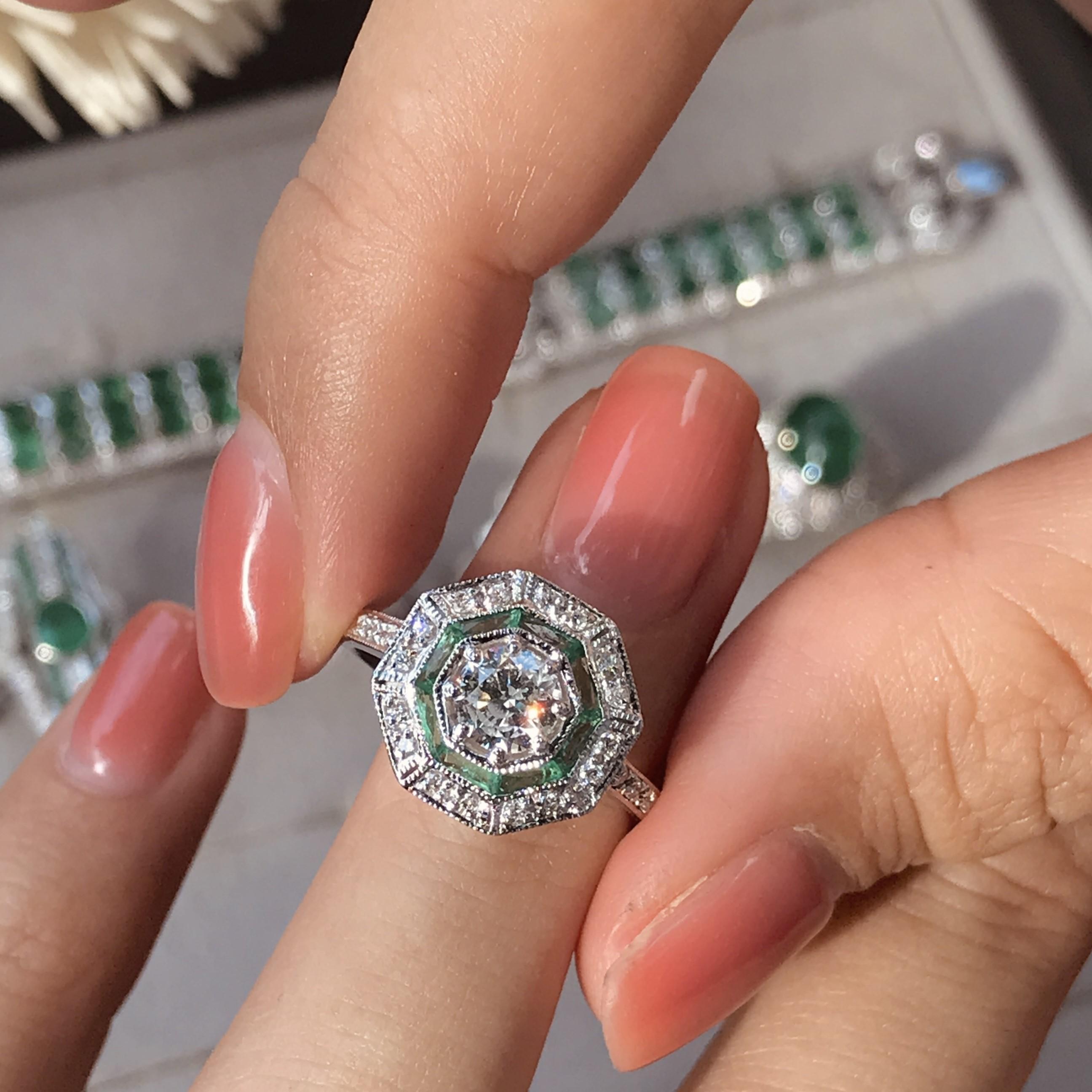 An 18k white gold Art-Deco design diamond and emerald target ring, center diamond with an outer ring of round diamonds an inner one of French cut emeralds and finished with millgrain edging, finished with diamond shoulders.

Ring Information
Style: