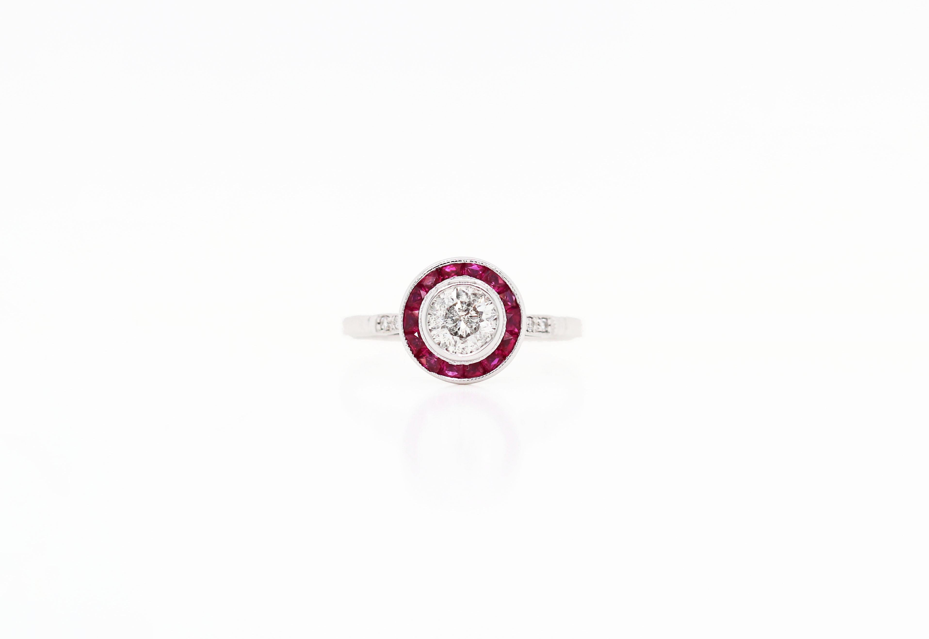 Art Deco style target engagement ring set with a round brilliant cut diamond weighing approximately 0.60ct in a rub over, open back setting in the centre of a beautiful  ruby grain set halo. The ring is further grain set with two round brilliant cut