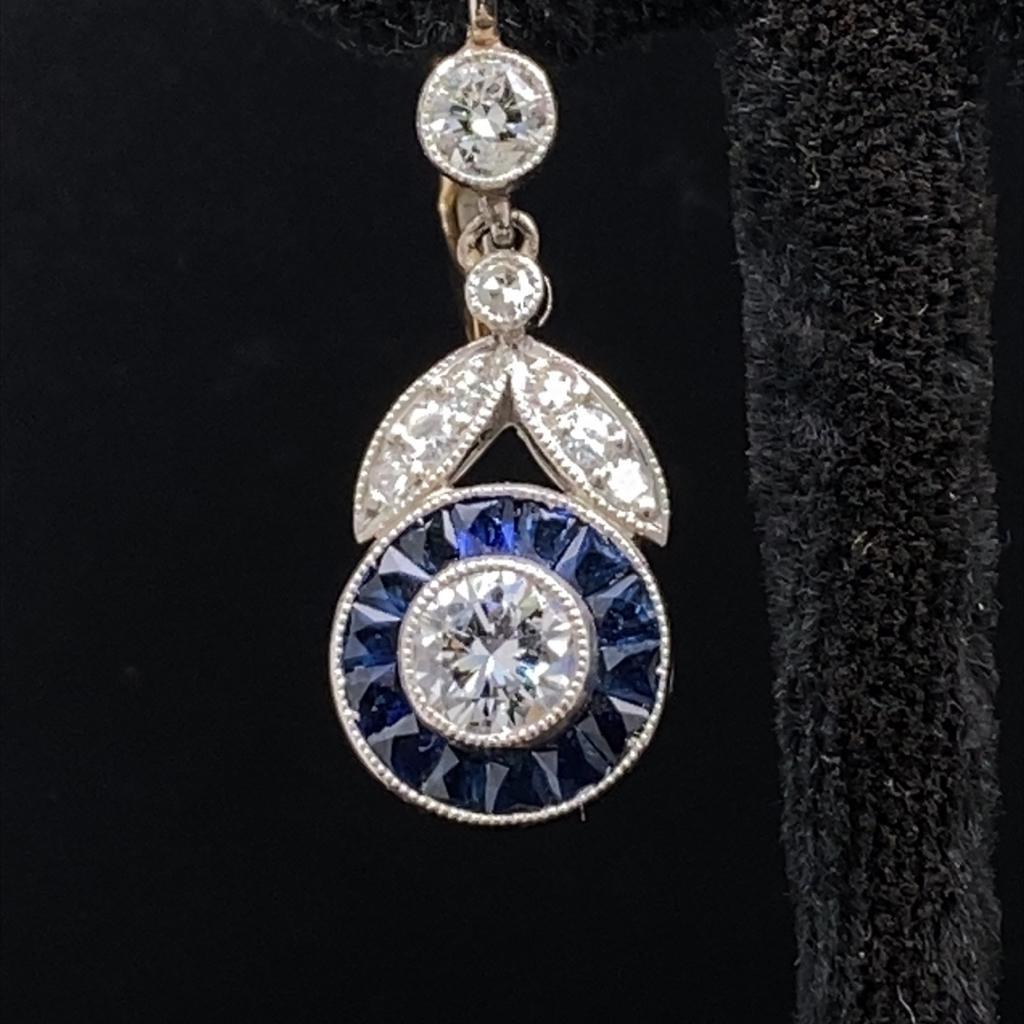 A pair of Art Deco style diamond and sapphire floral target earrings in platinum.

Each drop earring is set to its centre with a sparkly 0.25 carat old mine cut diamond in a rubover setting. An elegant target surround of calibré set French cut