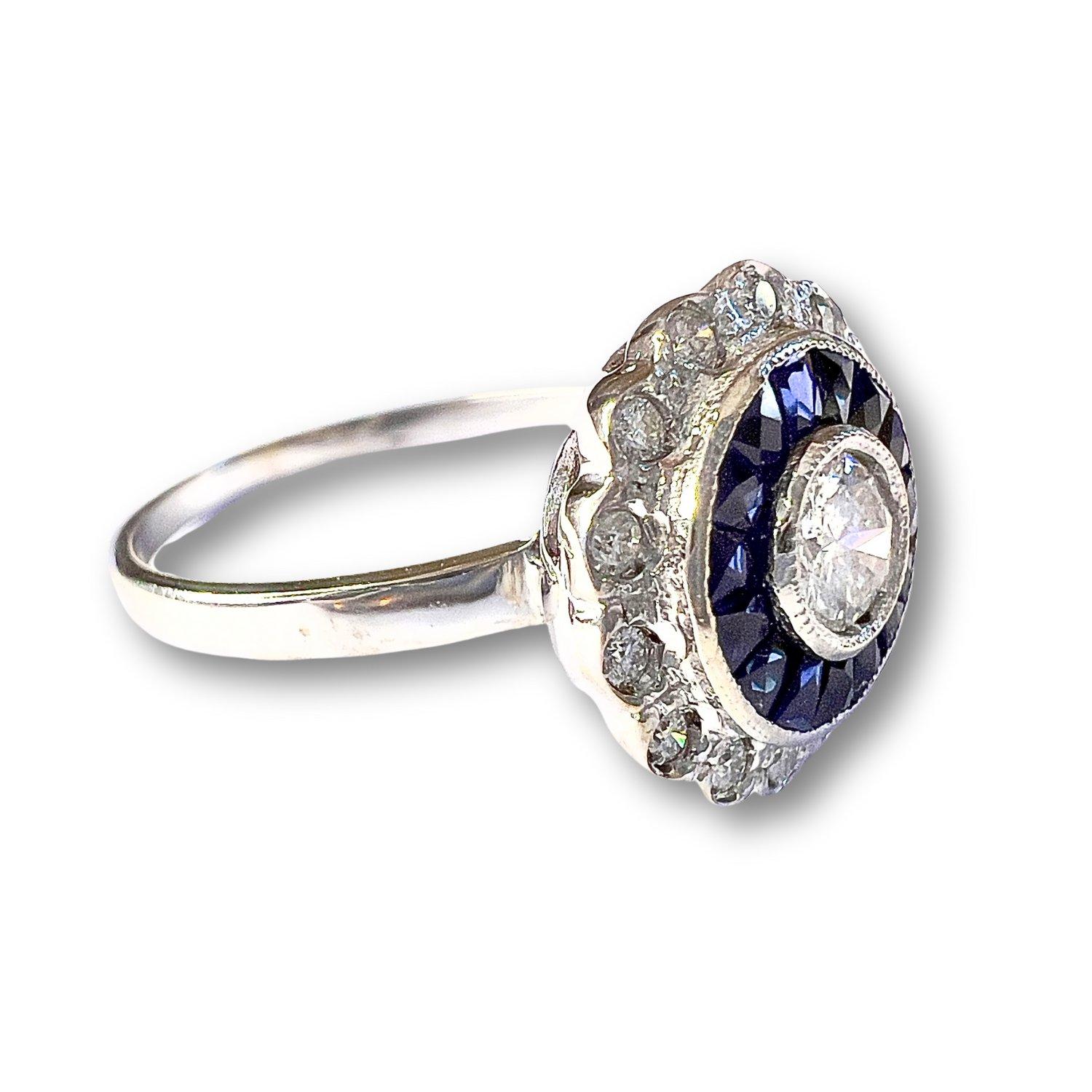 This ring captures the essence of the Art Deco style, crafted in 18K white gold. It features brilliant-cut Diamonds totaling 0.40 carats, with a central brilliant-cut Diamond weighing 0.76 carats. The ring also showcases antique trapezoid-cut