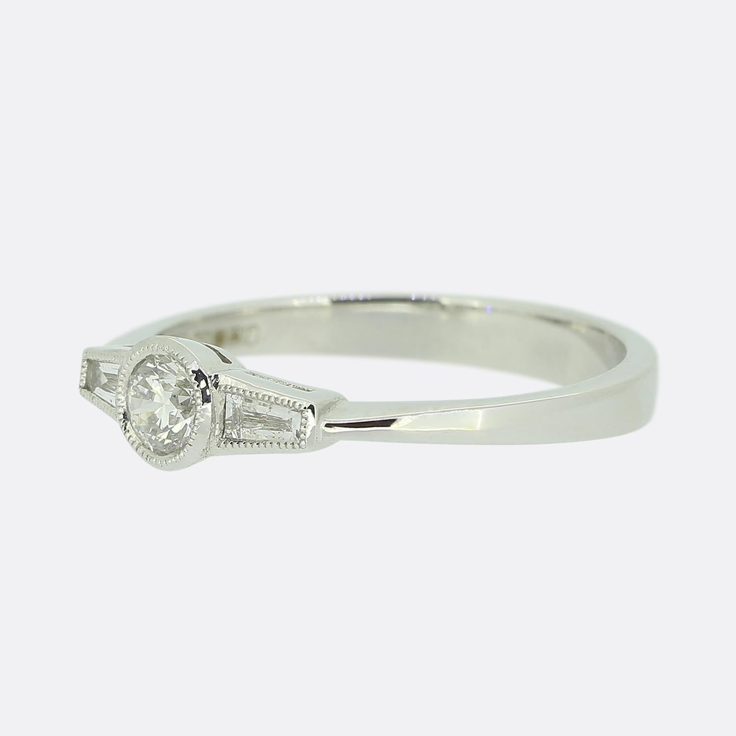 Ecco un dolce ed elegante anello con tre pietre di diamante in oro bianco 18ct. Un diamante rotondo a taglio brillante centrale è affiancato da due splendidi diamanti affusolati a taglio baguette, tutti racchiusi in un raffinato dettaglio