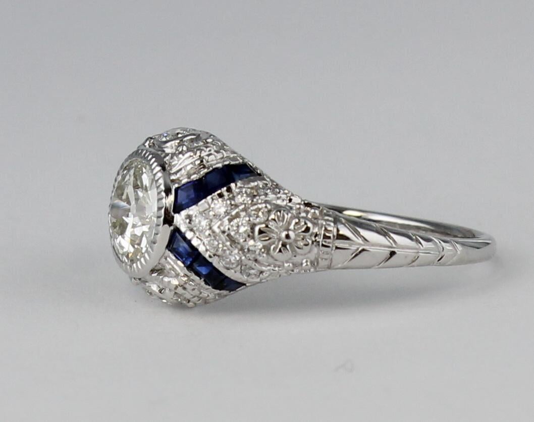A beautiful .80 carat diamond, VS 1 clarity, H color, is bezel-set in the center of this gorgeous 18 karat white gold Art Deco style ring.  There are .45 carat total weight of sapphires as well as pave-set diamonds enhancing the center stone.  This
