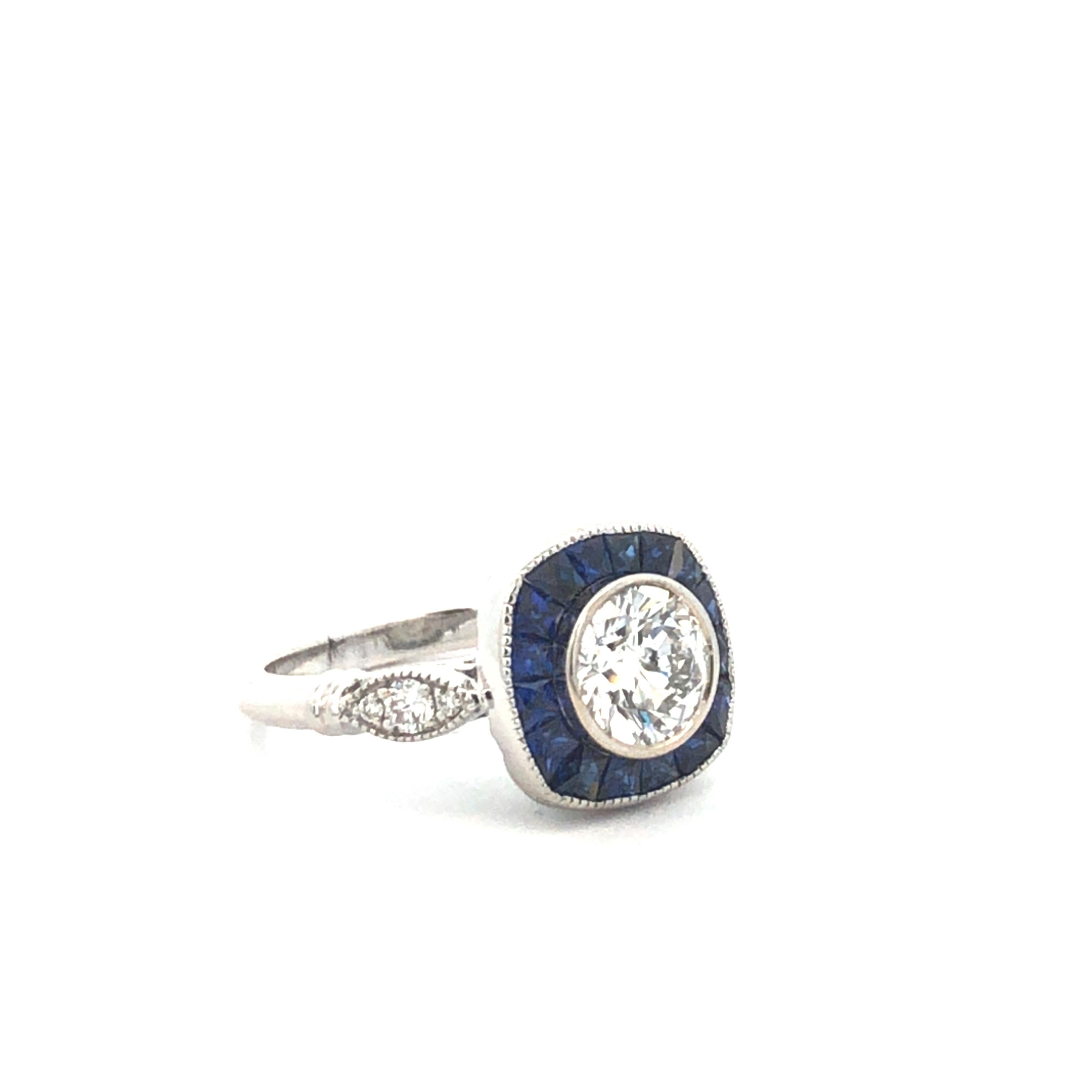 La pièce maîtresse est un diamant de taille brillant pesant environ 1,11 carat. Un halo de saphirs bleus l'entoure, ajoutant une touche de luxe et de contraste au design de la bague.  Le halo comporte 1,00 carat de saphirs bleus, méticuleusement