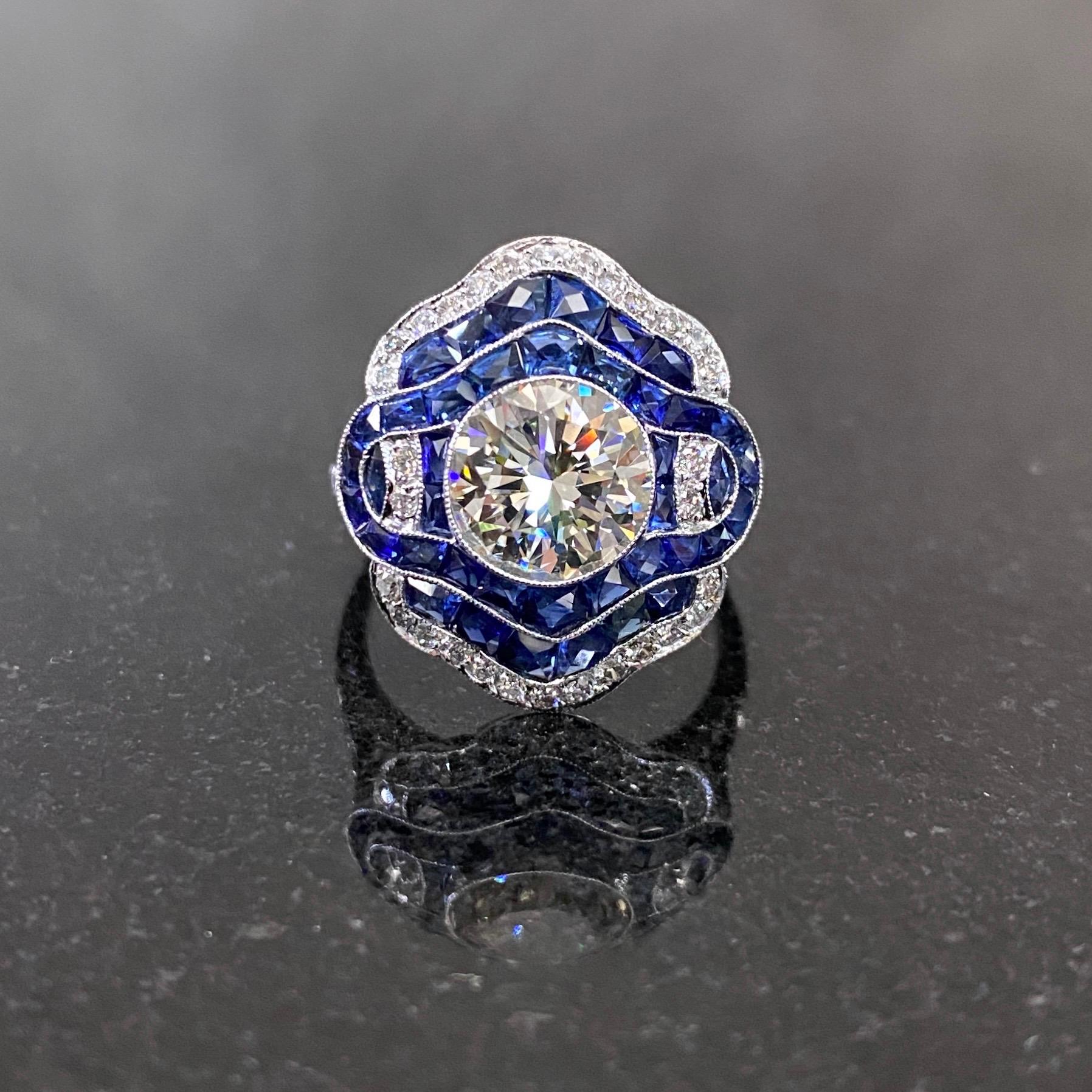 Art Deco Style diamond and sapphire target stylized engagement or cocktail/dress ring in platinum, 2000s. This ring features a round brilliant-cut diamond millegrain-set to the center, surrounded by several rows of channel-set and grain-set