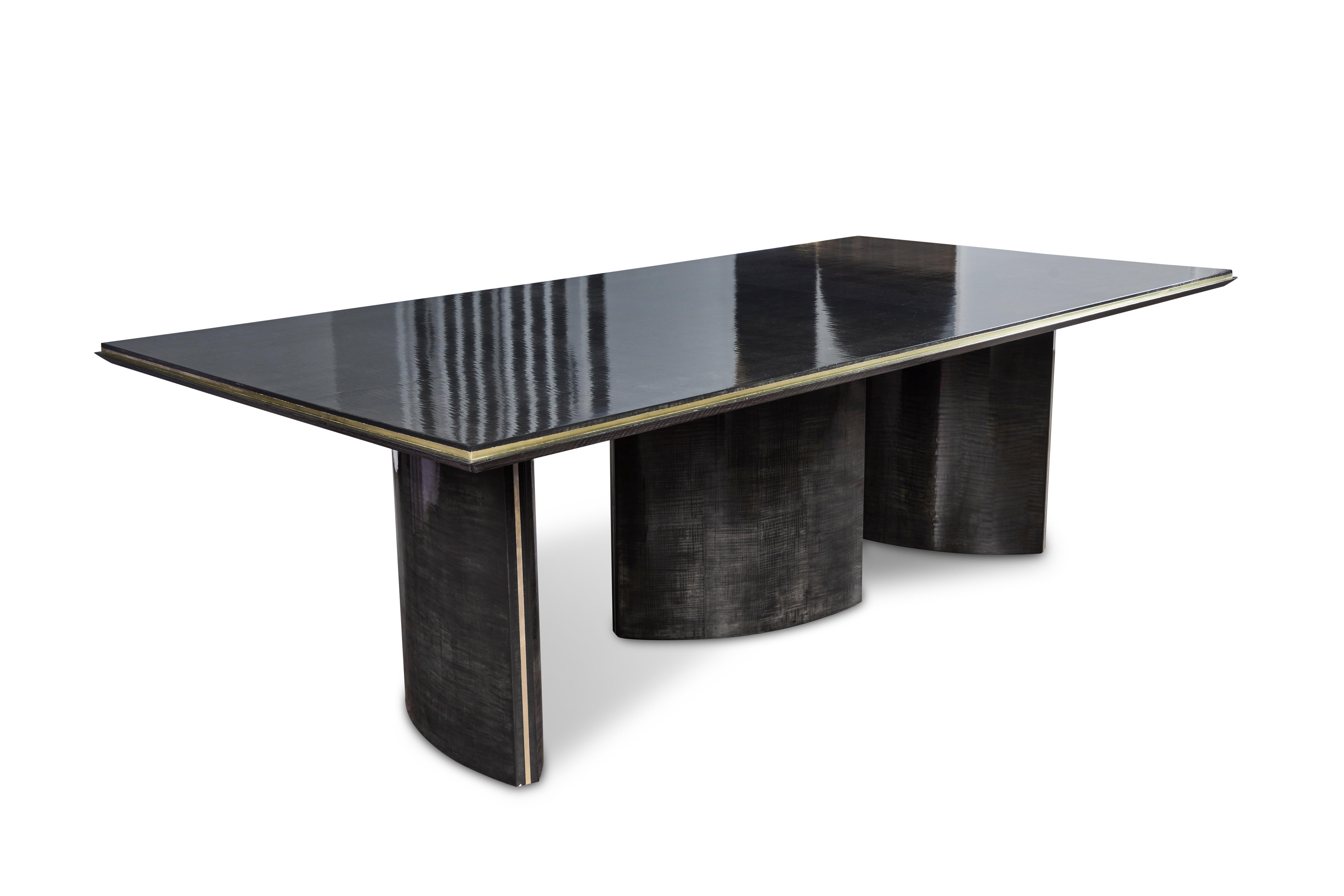 Chic and elegant dining table mad of lacquered sycamore with brass metal detailing. Table features three ovoid bases with brass detailing on the sides, positioned at different angles, supporting the table top with brass detailing all around the