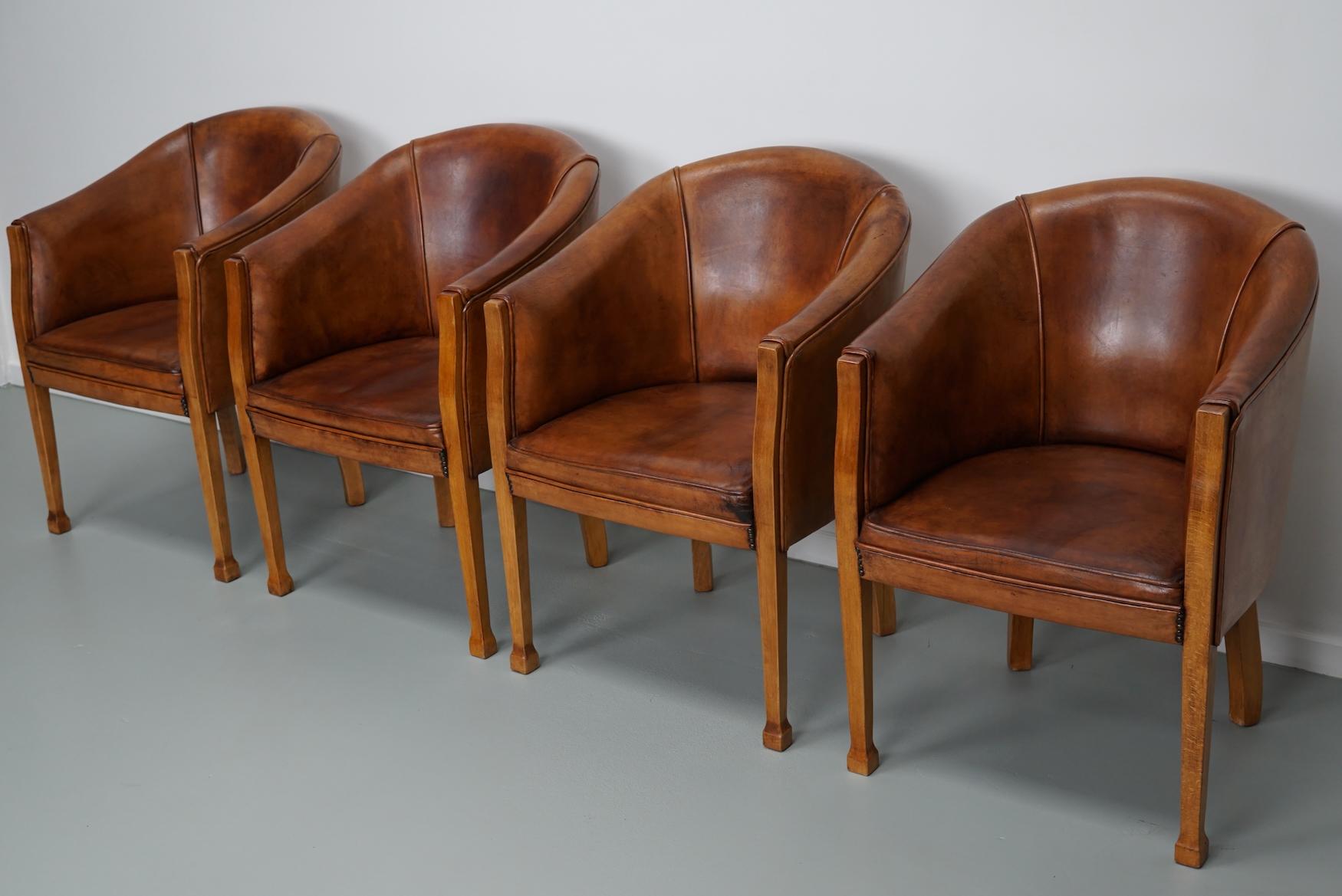 This set of four cognac-colored leather club chairs come from the Netherlands. They are upholstered with cognac-colored leather and feature metal rivets and wooden legs. 