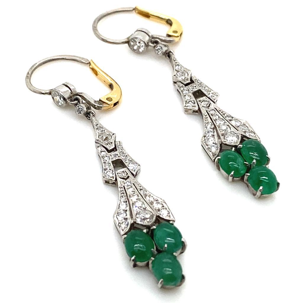 A pair of Art Deco style emerald and diamond drop earrings in 14 karat white and yellow gold.

Each earring features a trio of cabochon cut emeralds suspended from three beautifully articulated diamond sections, set to the top of the drop with two
