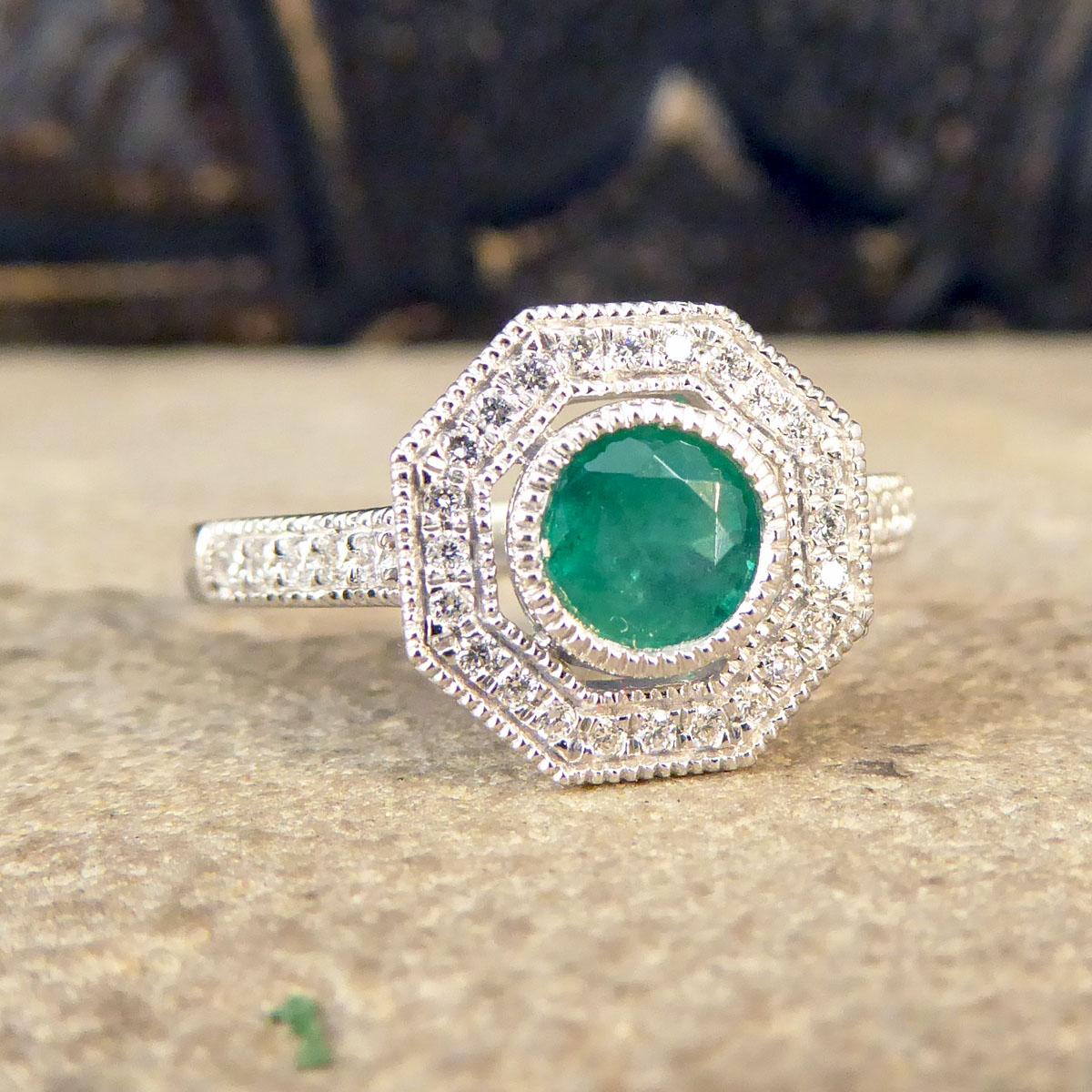 Known for its association with geometric lines and angles this Contemporary ring has been crafted in an Art Deco Style. The Round Cut Emerald that centres this ring weighs 0.30ct held into place with a milgrain rub over setting. Clustering this