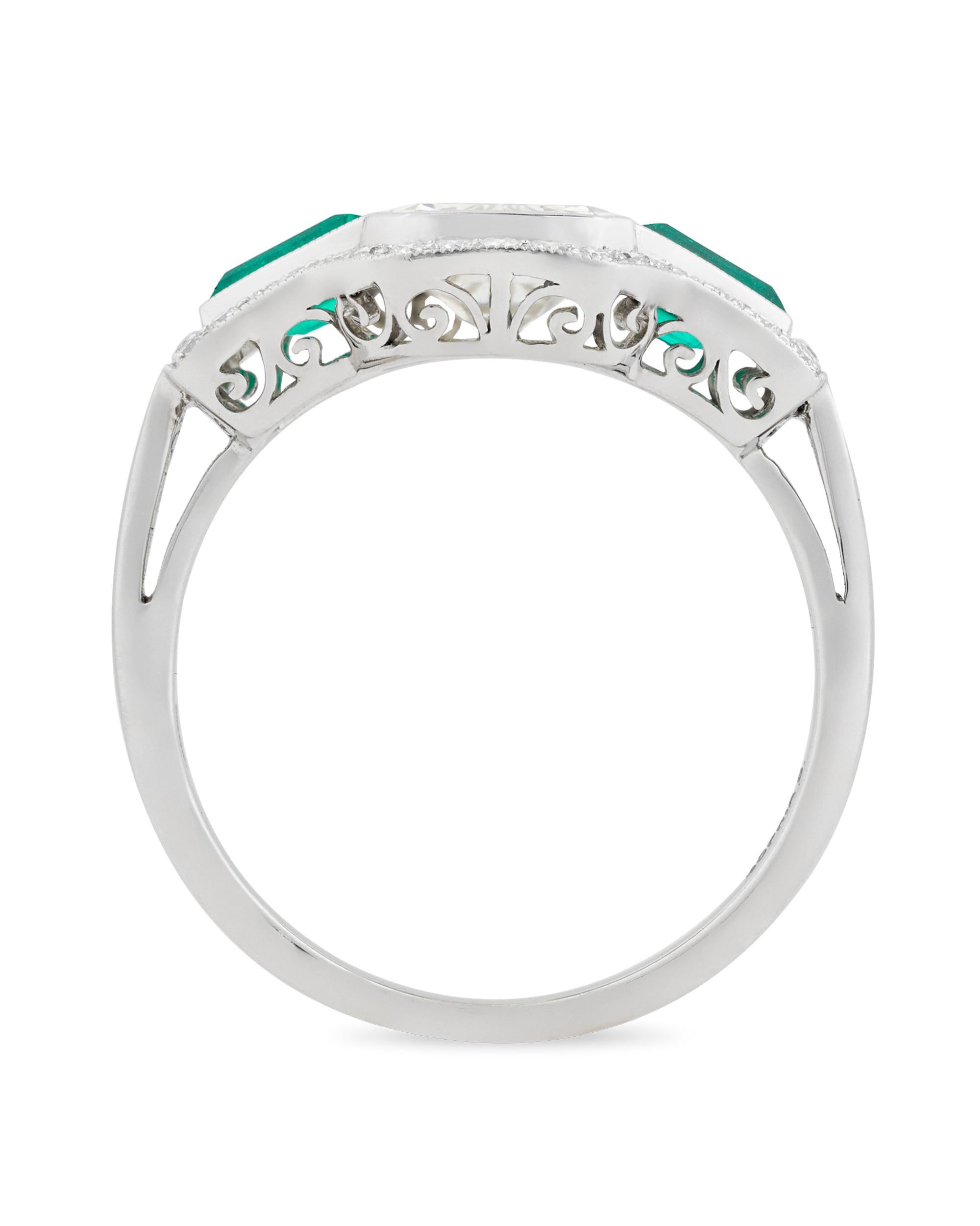 Art Deco-era elegance is perfectly reflected in this emerald and diamond ring. The 1.86-carat emerald-cut center diamond is boldly flanked by two emeralds totaling 0.64 carat and bordered by an additional 0.23 carat of diamond accents. The striking,