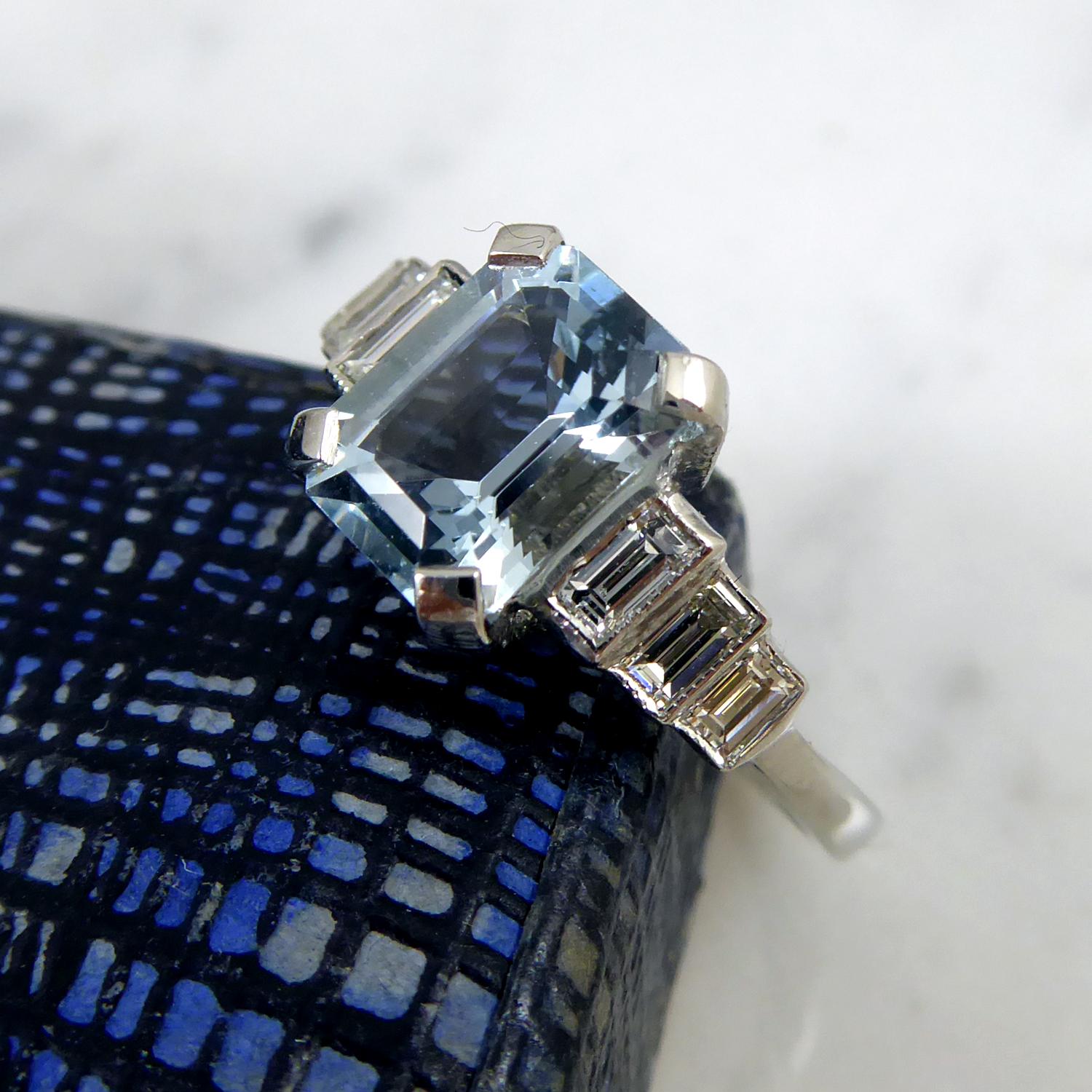 Art Deco Style aquamarine and diamond ring set with an emerald cut aquamarine of mid-blue colour in a four claw setting.  Weight approx. 1.40ct, the aquamarine is set on shoulders each set with three baguette cut diamonds in rub over settings. 