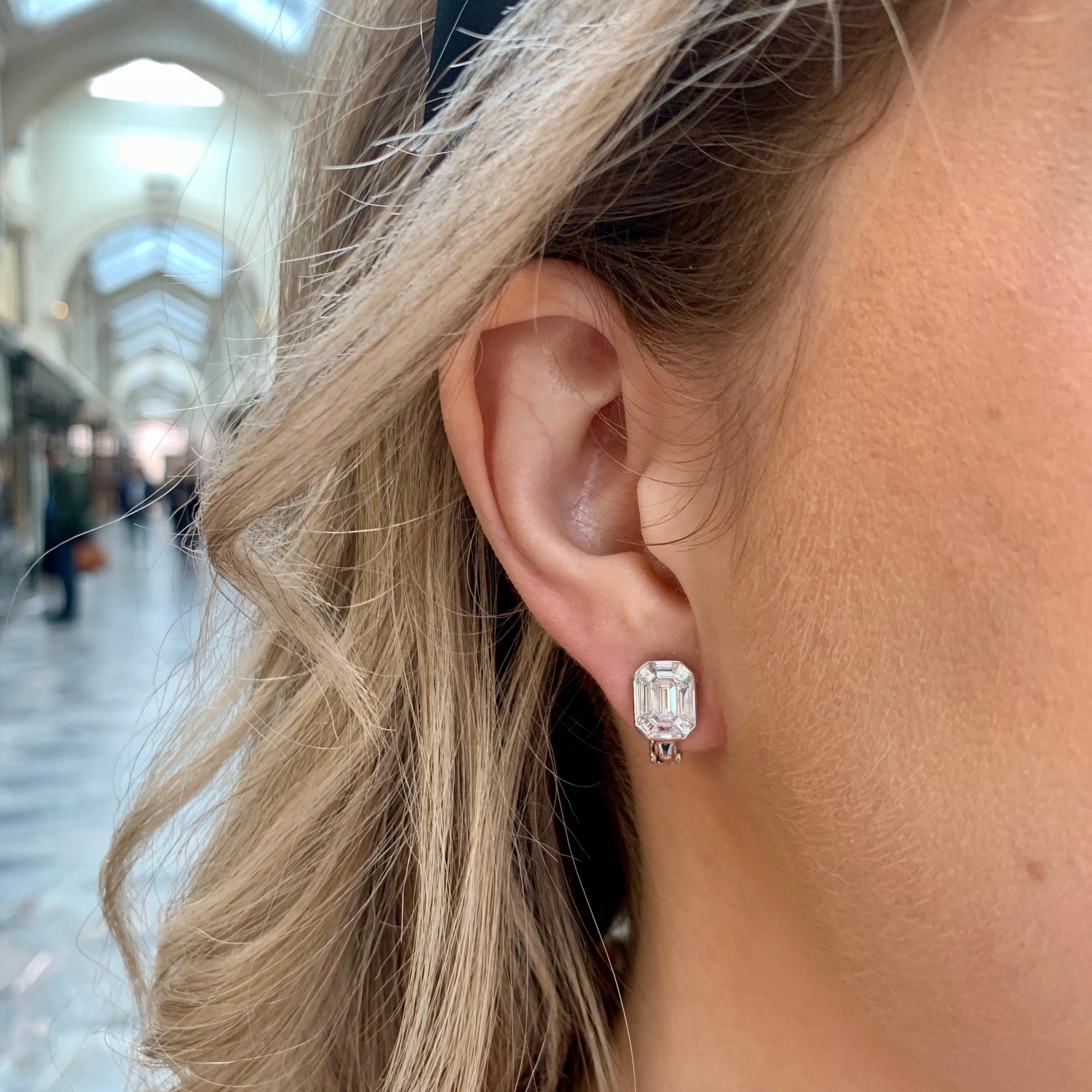  A beautiful pair of emerald cut diamond cluster earrings set in platinum. 

Each earring is centrally set with a sparkly emerald cut diamond which is set amongst a surround of 8 calibre step-cut diamonds. All the stones are set in a rub-over