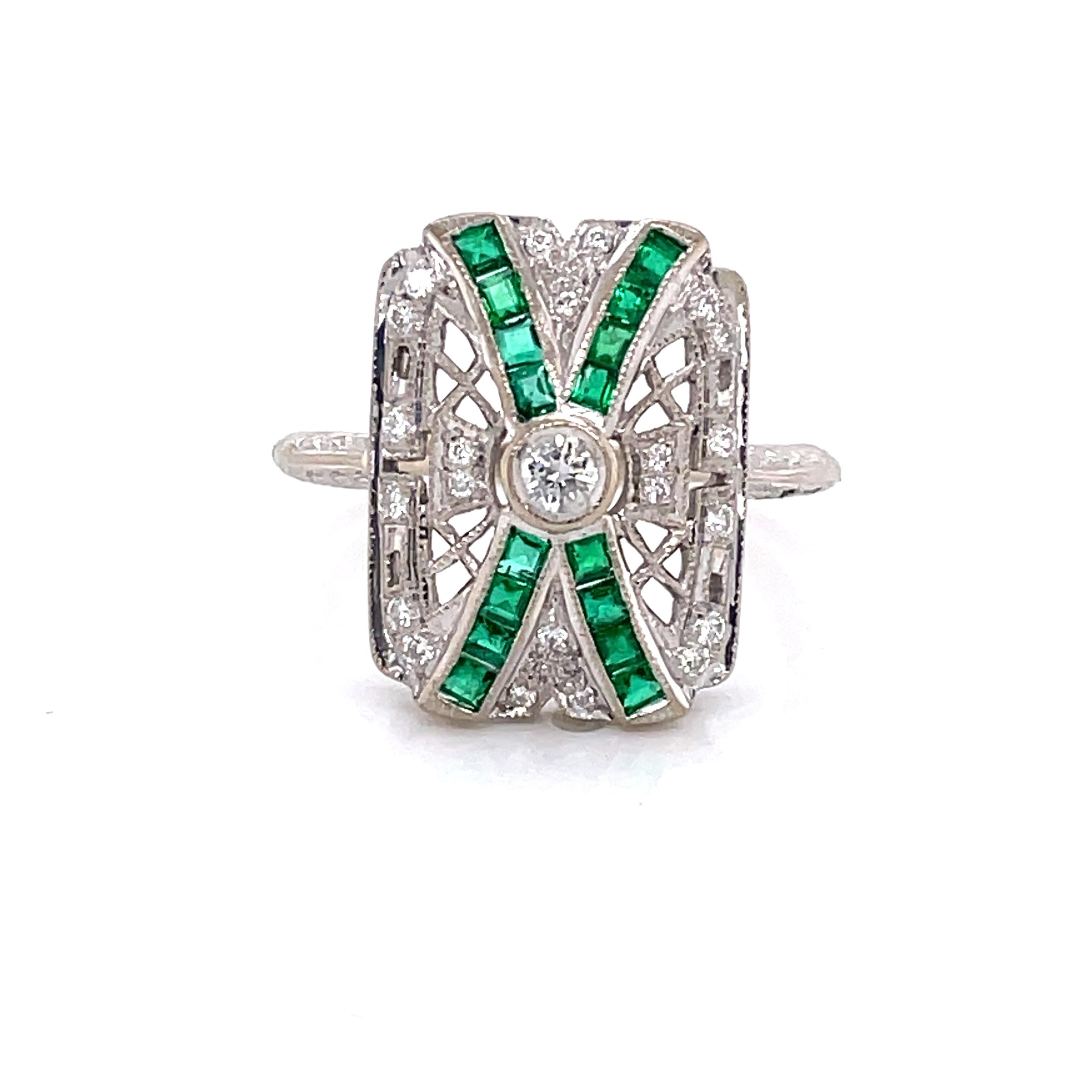 Vibrant emerald ribbons cross atop of the diamond covered eighteen karat 18K white gold filigree head of this stunning Art Deco style ring making it a great choice for antique style lovers or as a unique engagement ring. A round full cut .10 carat