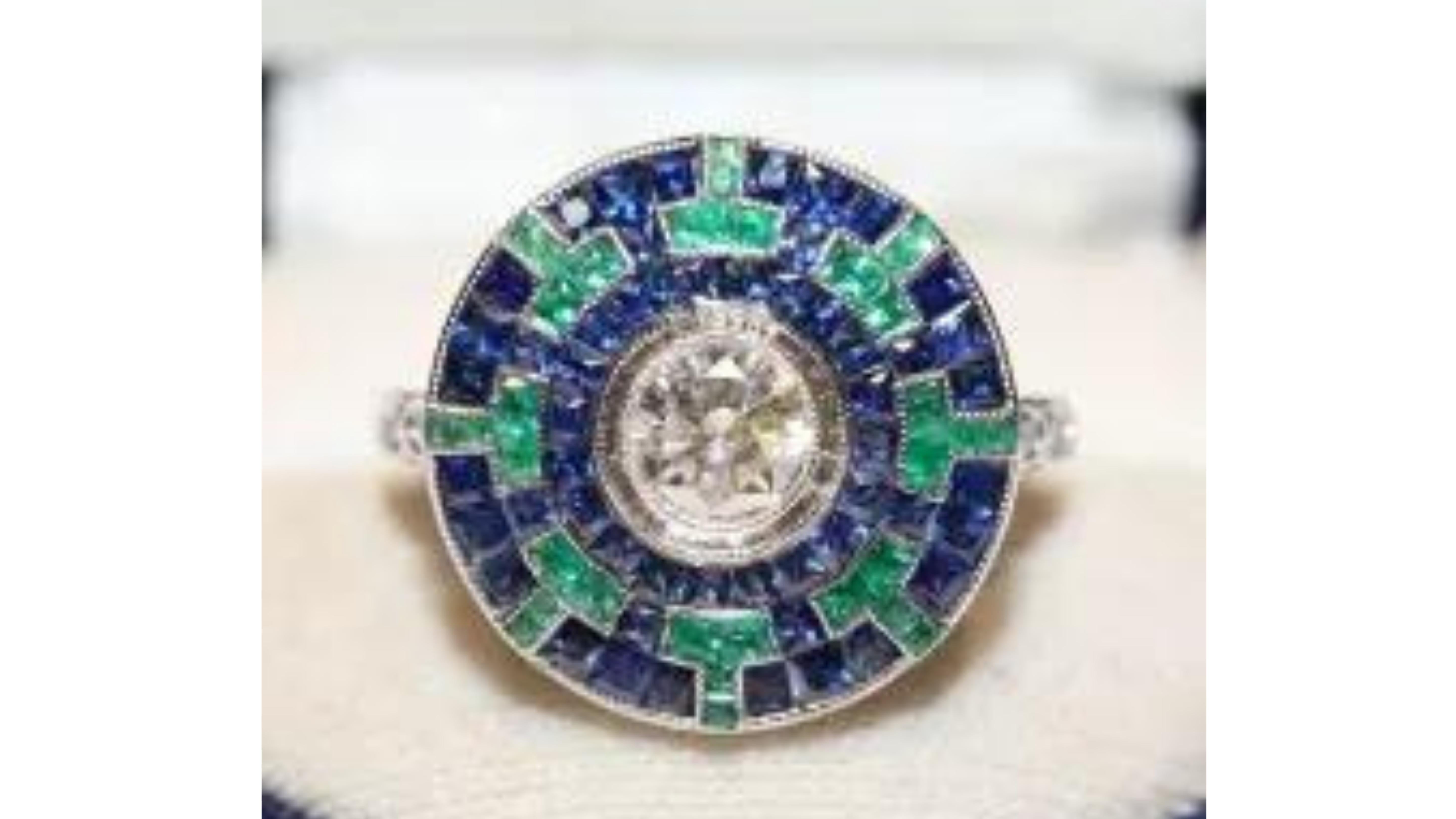 Art Deco Style Emerald Sapphire Diamond Ring 18k White Gold

This unique ring stands out with 32   Blue Sapphires  28  Emeralds wit a White Diamond in centre . This can also be made with other stones too and notice the diamonds down side of the ring