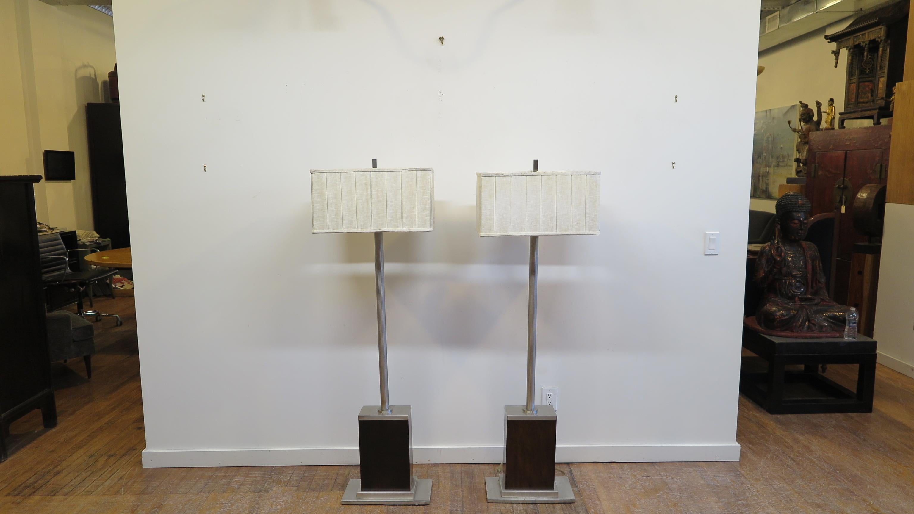 Pair of Art Deco style floor lamps. Brushed aluminum, poles are reeded, set into large wood blocks on metal plinth bases. In good condition. Each lamp having two sockets. Lamps are heavy each weighing about 35lbs. In very good condition.  New shades