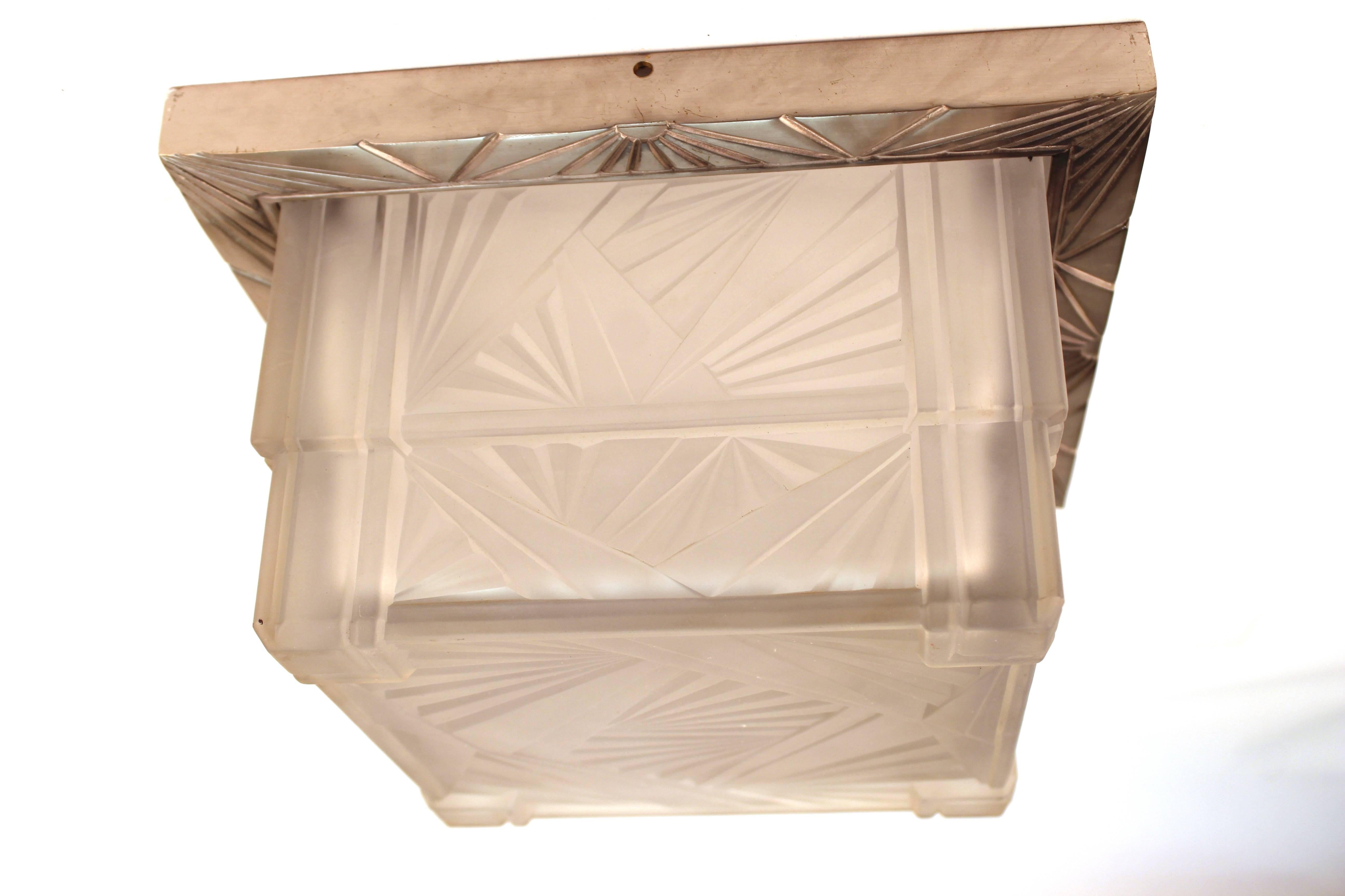 Art Deco flush ceiling fixture with silver-tone metal mount. The ceiling light features a two-tier square centre in cut frosted glass. The glass and metal mount feature geometric radiating patterns throughout. The fixture accepts two-light bulbs.