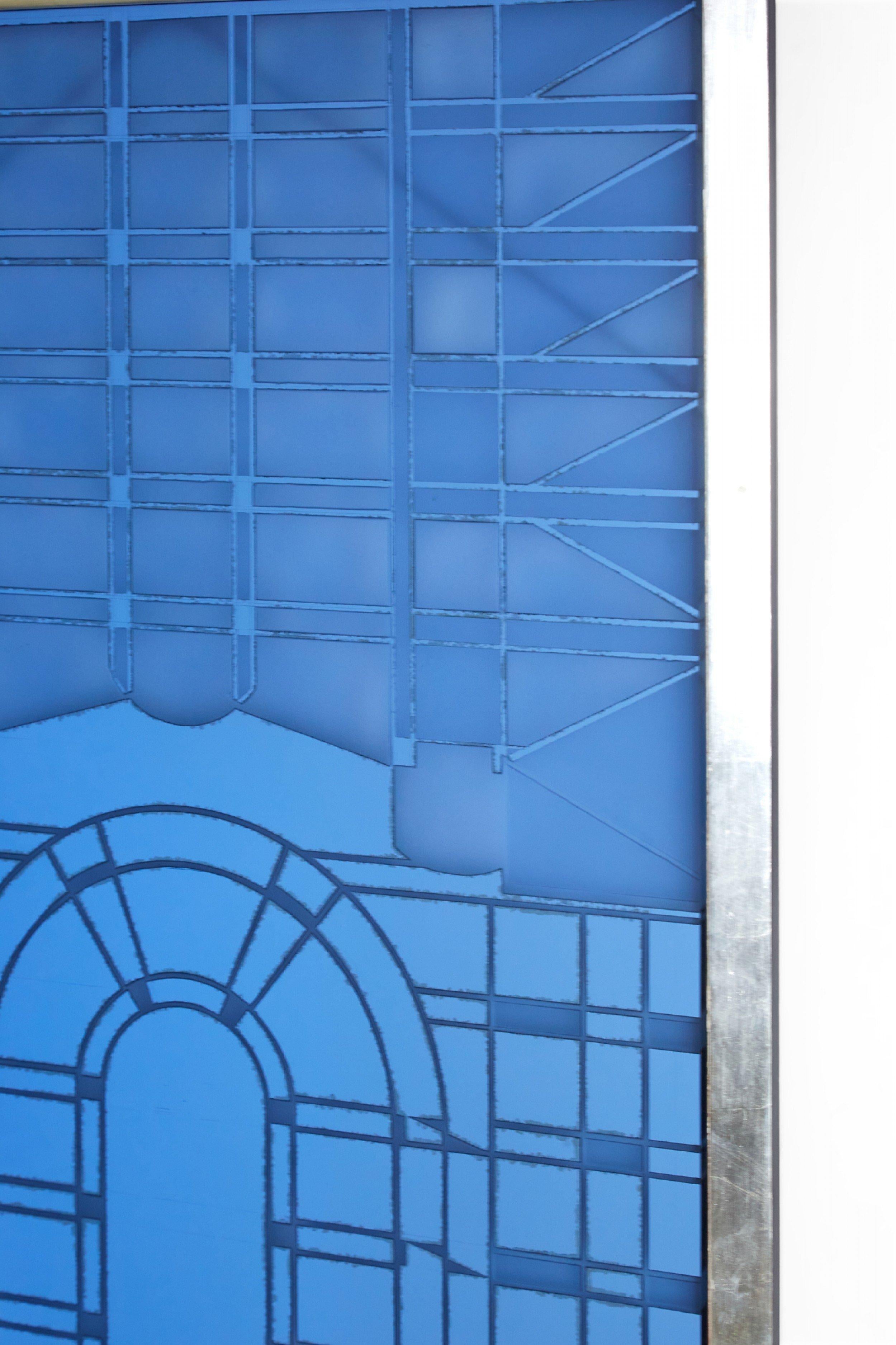 American Art Deco-Style framed glass mirror panel featuring geometric designs in blue and silver in a rectangular silver leaf frame.
 
