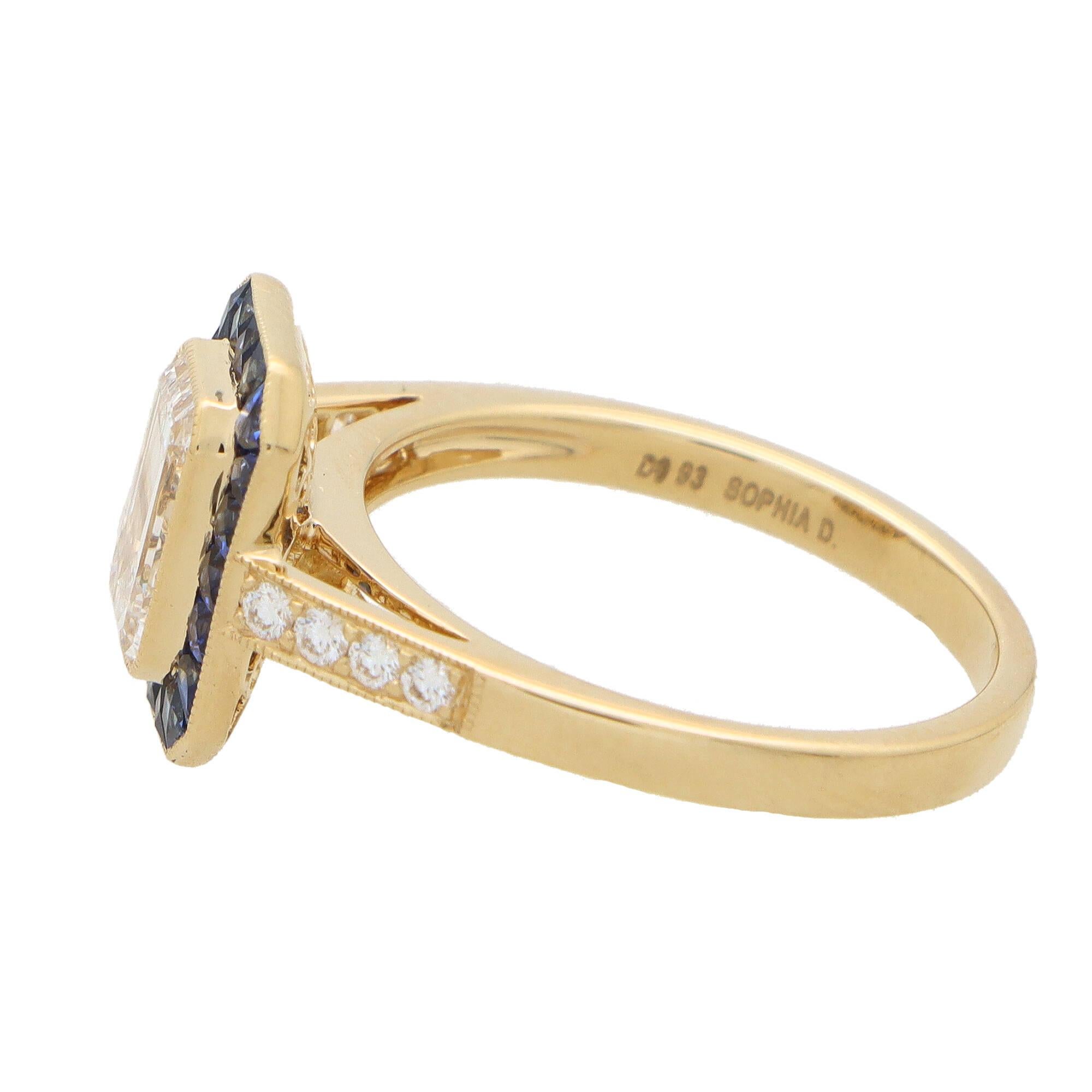 A rather unique Art Deco inspired GIA certified sapphire and diamond target ring set in 18k yellow gold.

The ring is predominantly set with a sparkly GIA certified D-coloured emerald cut diamond which is bezel set securely to centre. Surrounding